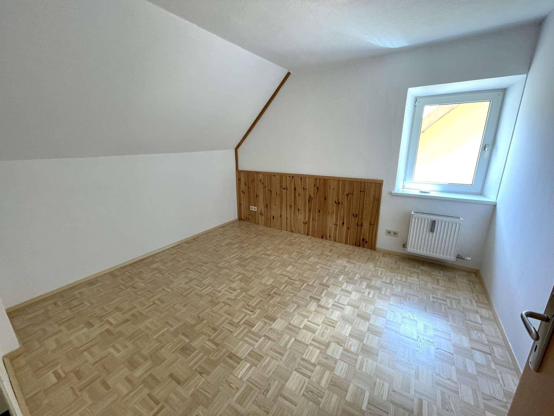 Schlafzimmer mit Parkettboden, Dachschräge und Holzverkleidung an einer Wand.