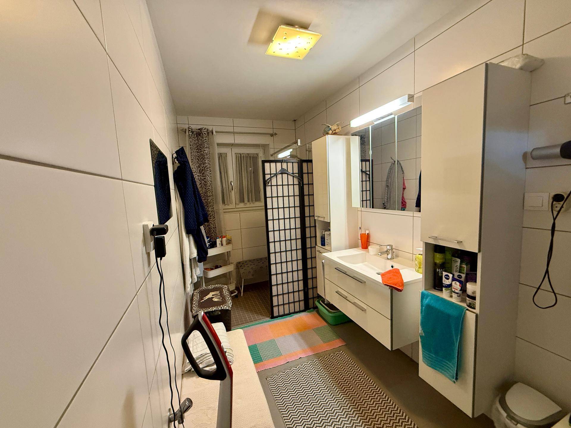 Helles Badezimmer mit weißem Waschbecken, Spiegelschrank und Duschbereich.