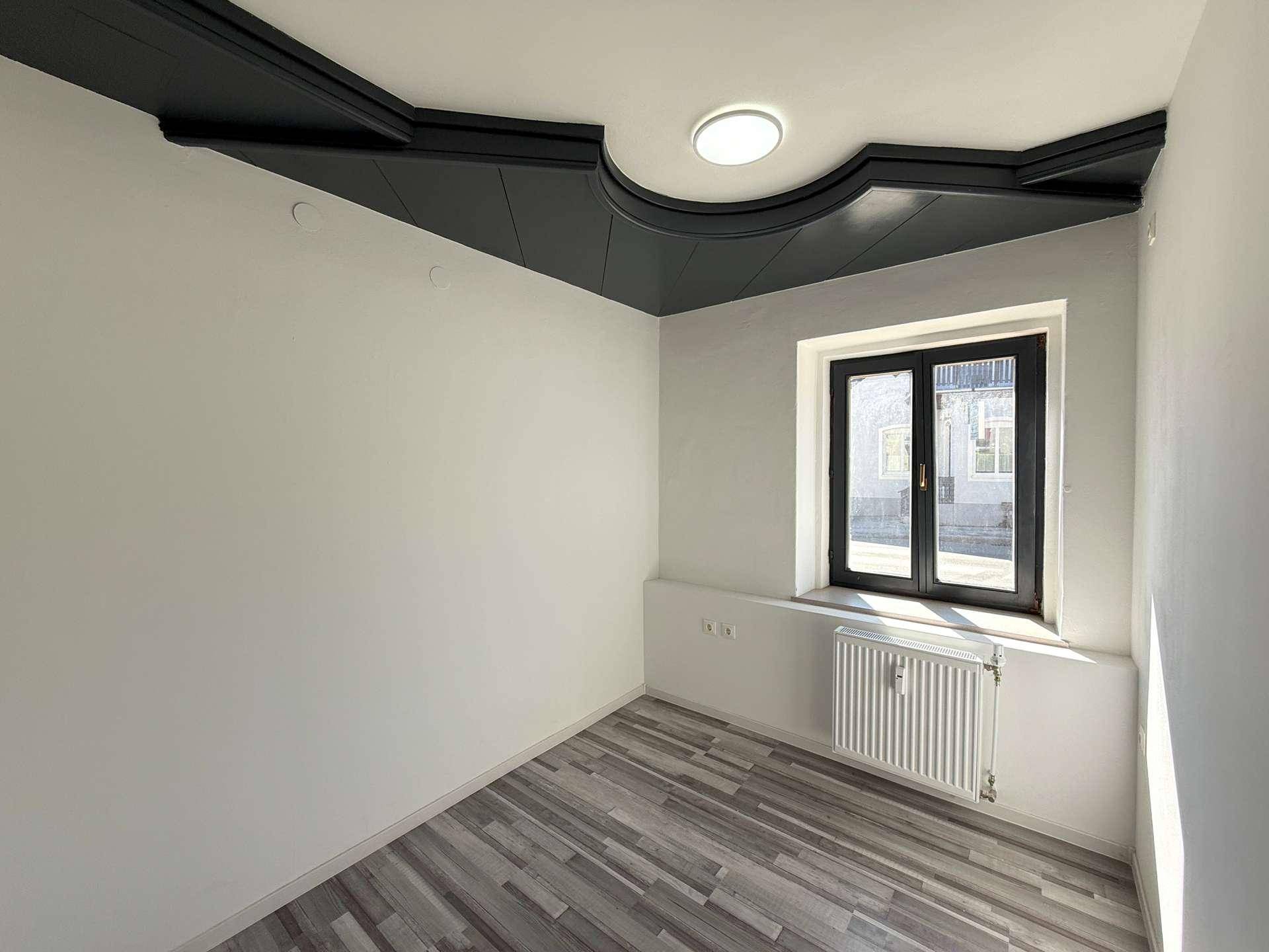 Zimmer mit Laminatboden, weißen Wänden und einer dekorativen dunklen Deckenleiste mit Beleuchtung.