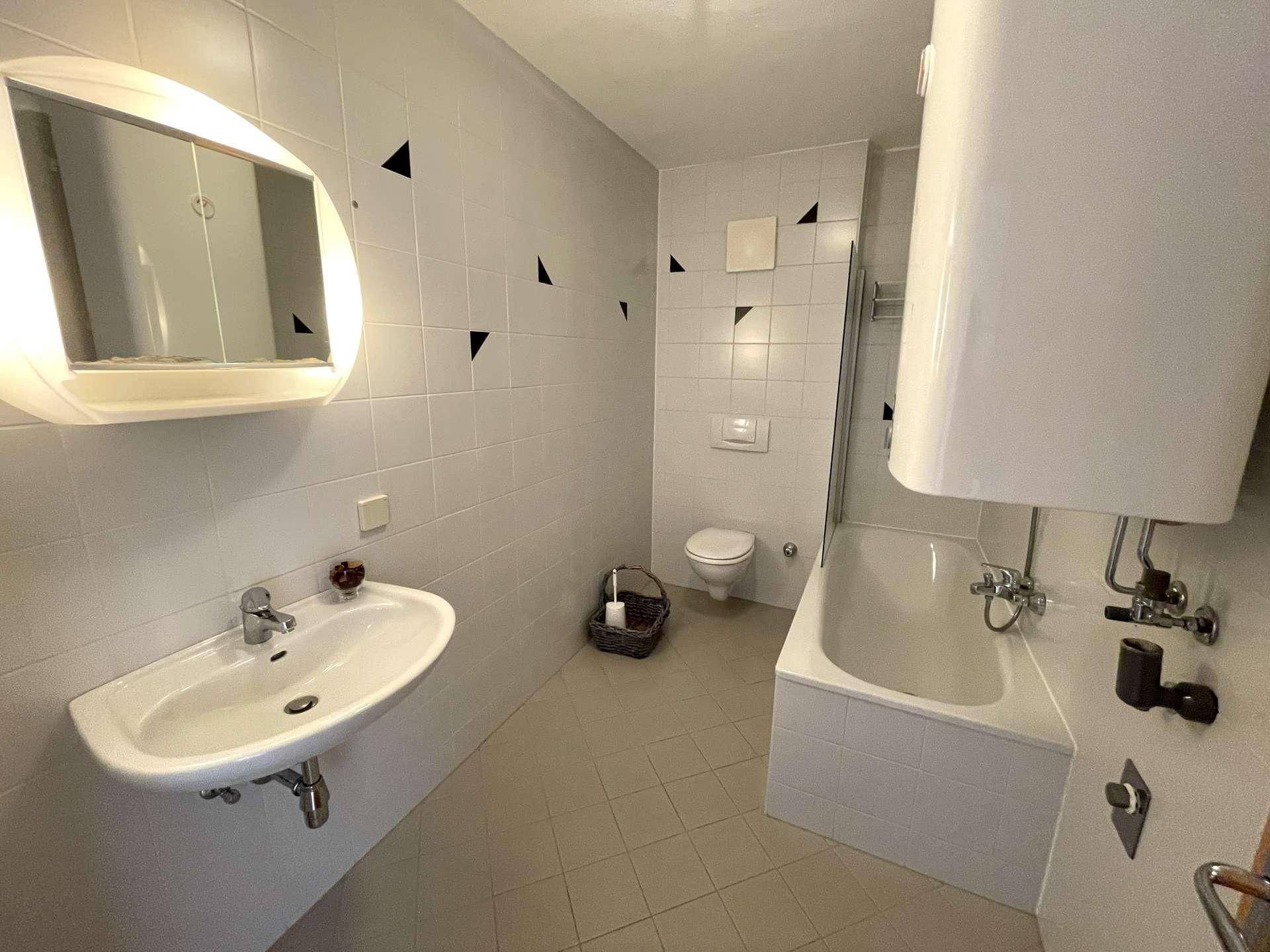 Badezimmer mit Badewanne, Waschbecken, WC und Wandfliesen mit geometrischem Muster.