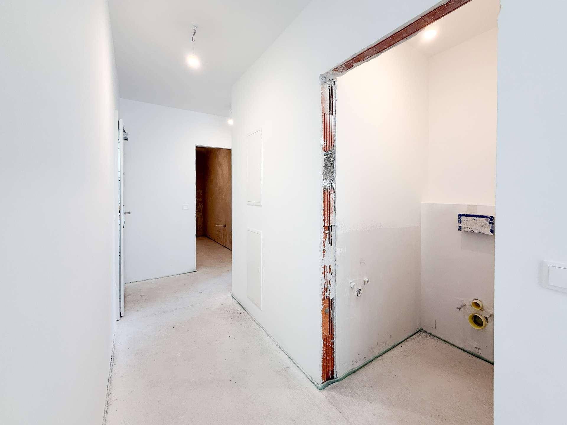 Heller Flur im Rohbau mit Zugang zu weiteren Räumen und einem unfertigen Badezimmer.