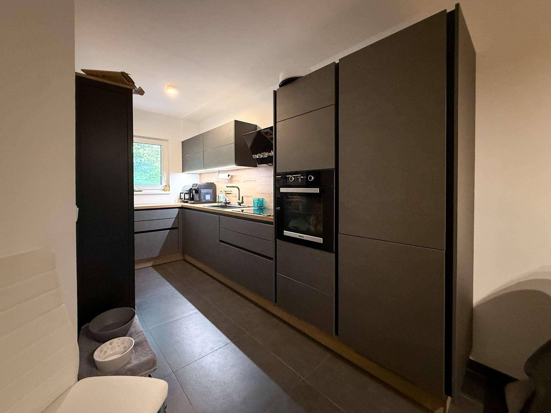 Moderne Küche mit dunklen, grifflosen Schränken, integrierten Geräten und Fenster.