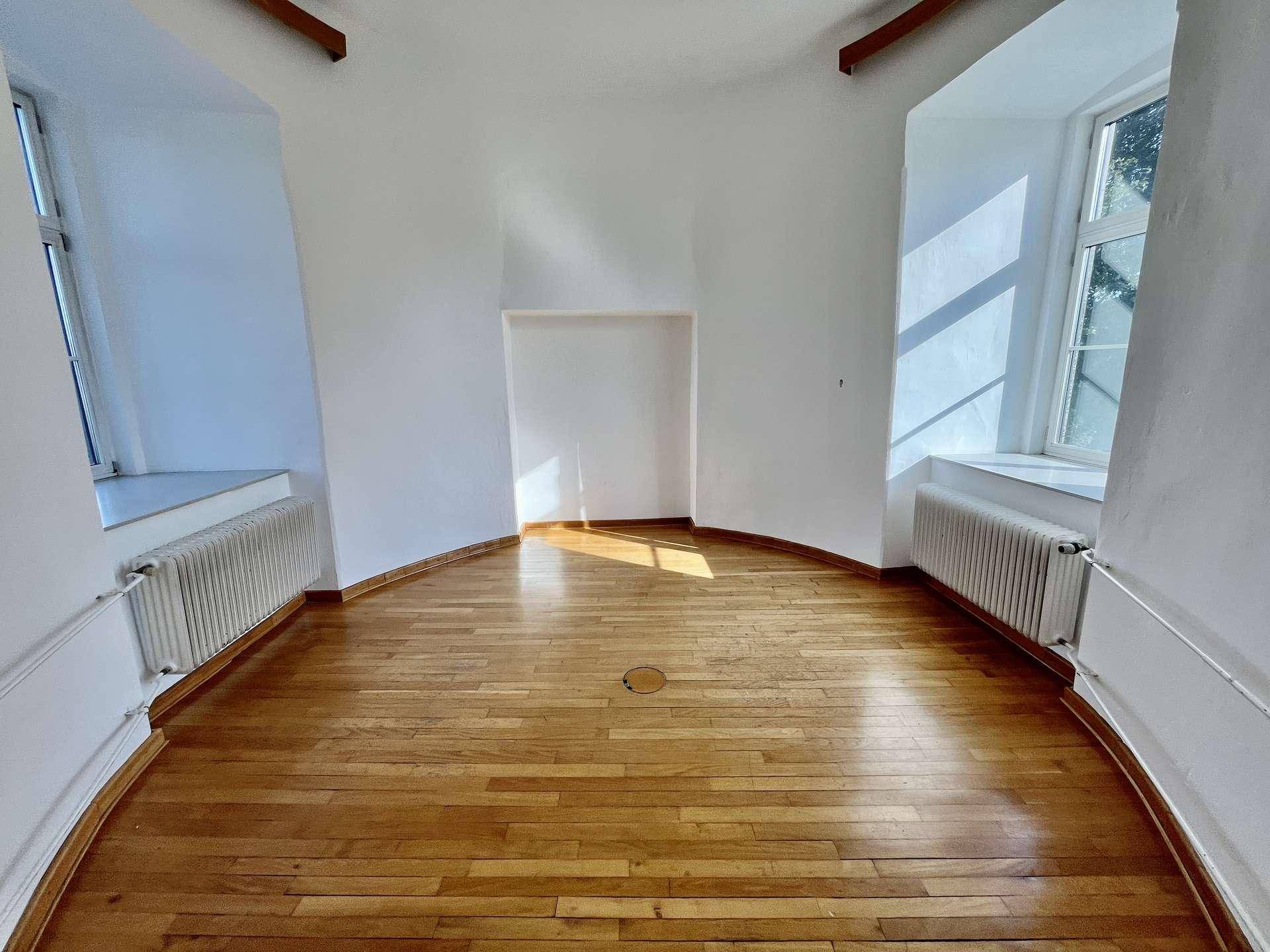 Heller Raum mit Holzboden, zwei Fenstern mit tiefen Laibungen und einer Nische.