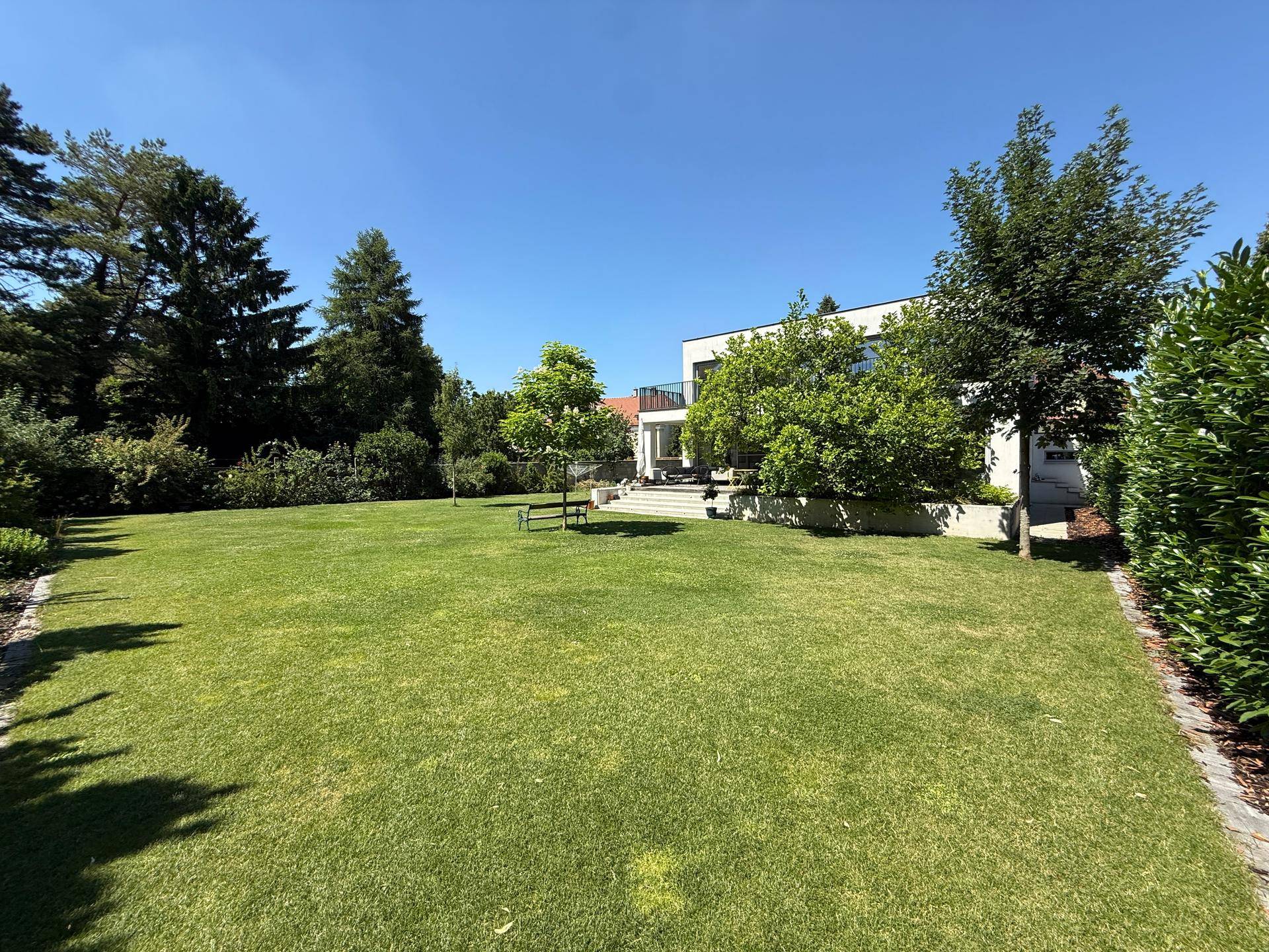 Großer, gepflegter Garten mit Rasenfläche, Bäumen und Blick auf die moderne Hausfassade.