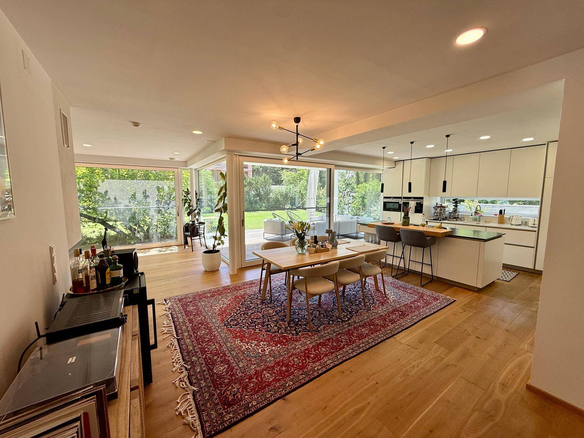 Offener Essbereich mit Holztisch, Teppich und Blick auf die moderne Küche und den Garten.