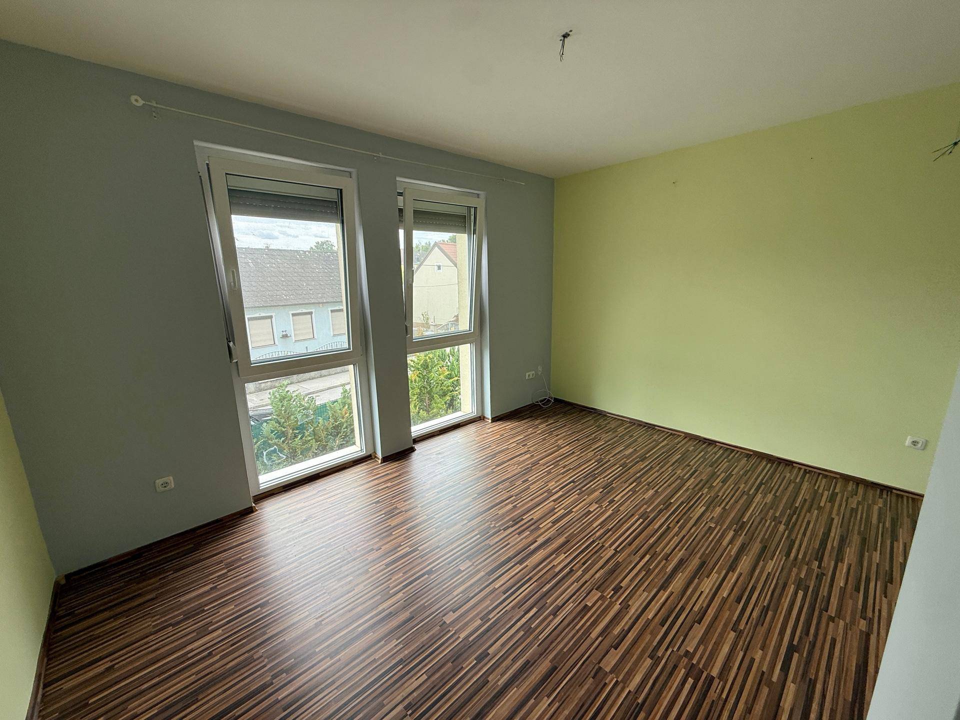 Schlafzimmer mit Laminatboden, großen Fenstern und Wänden in Grün- und Grautönen.
