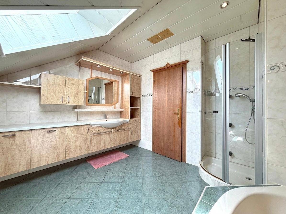Geräumiges Badezimmer mit Waschtisch, Duschkabine, Dachfenster und hellen Fliesen im Dachgeschoss.