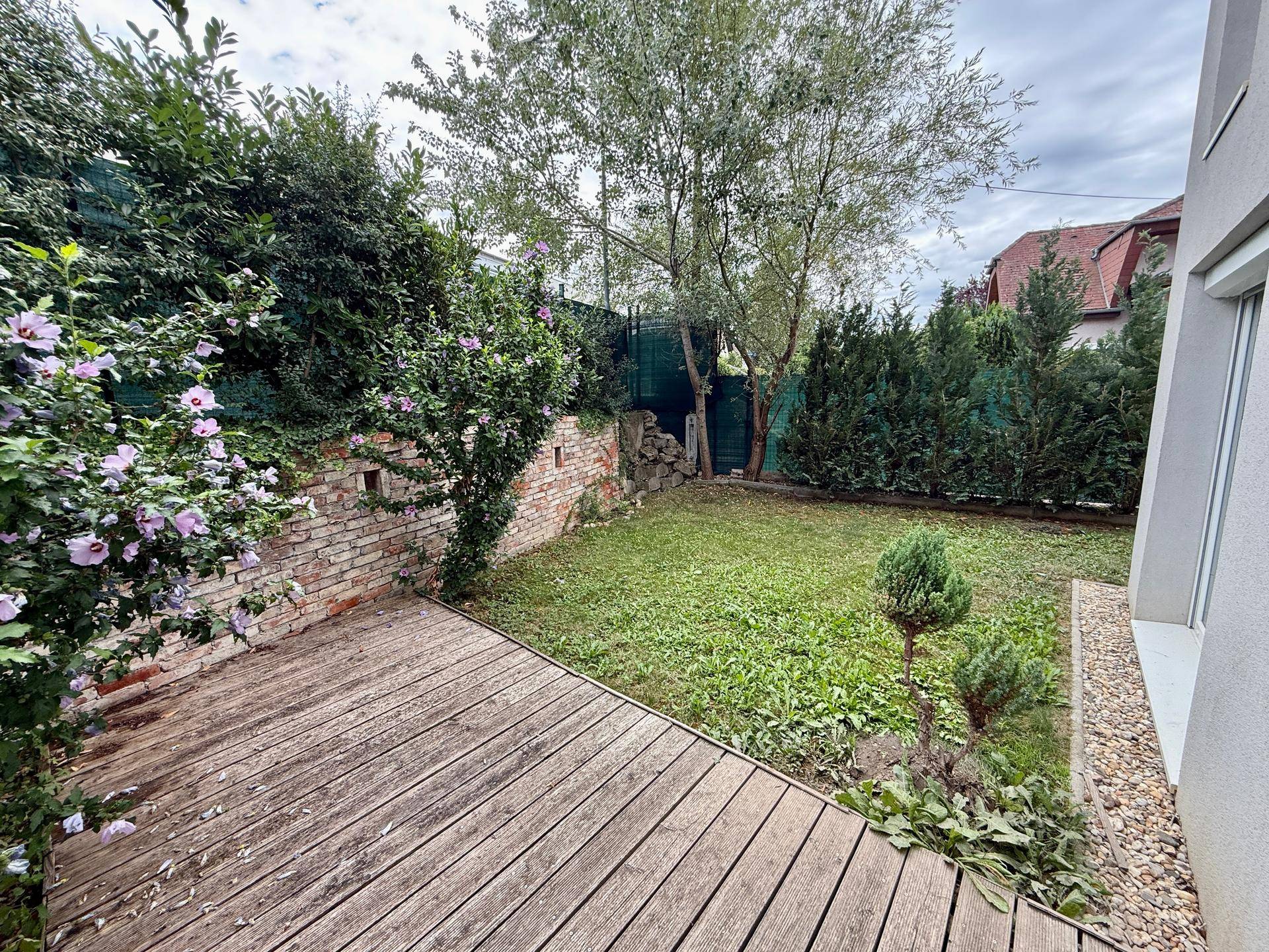 Ruhiger Gartenbereich mit Holzterrasse, Rasen und hohen Hecken für Privatsphäre.