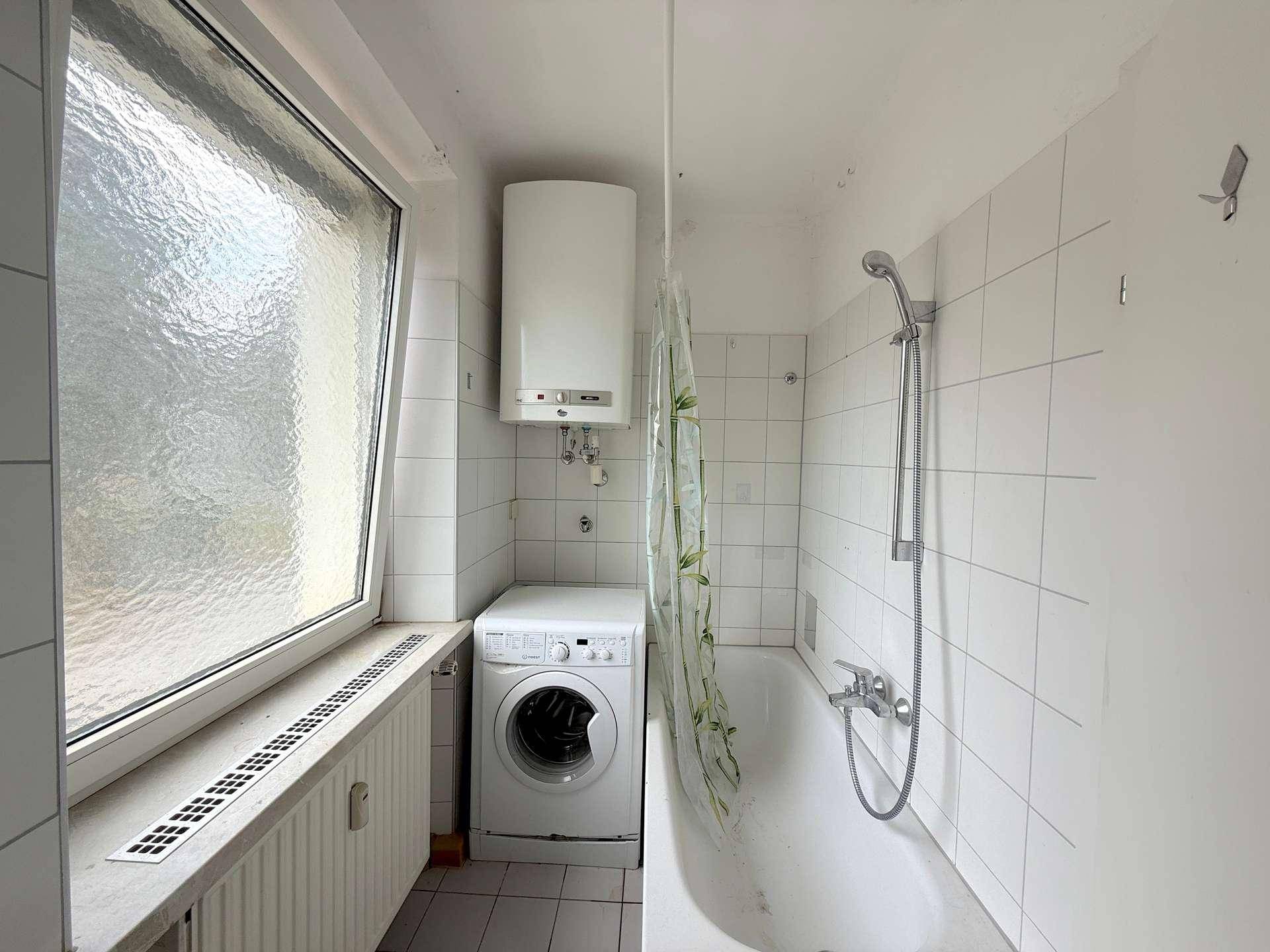 Badezimmer mit Badewanne, Duschvorhang, Waschmaschine und Fenster.