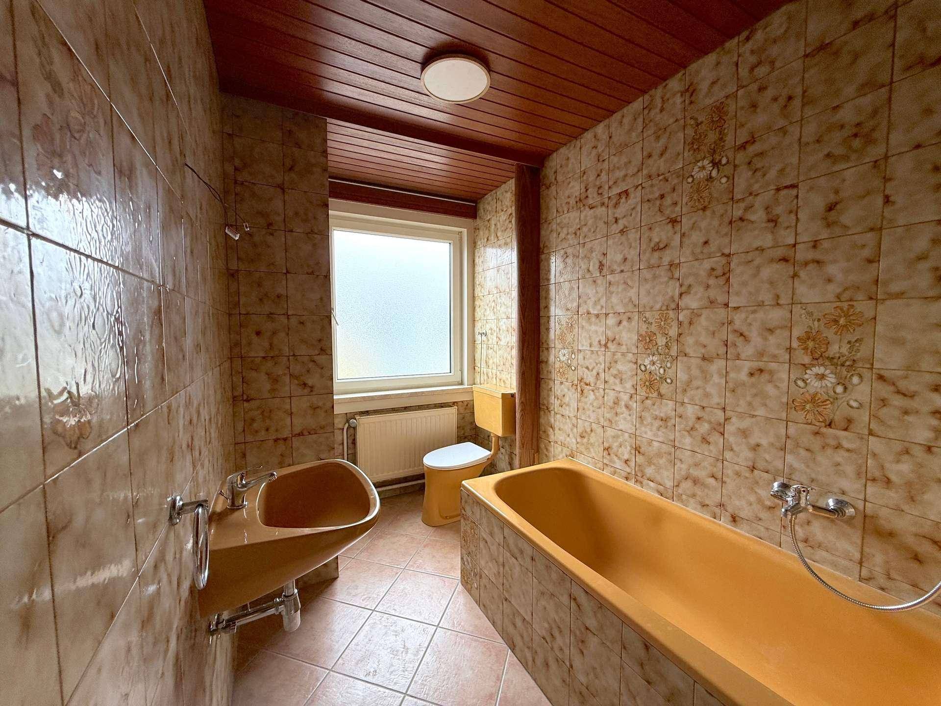 Badezimmer im Stil der 80er Jahre mit braunen Fliesen, passender Sanitärausstattung und Holzdecke.