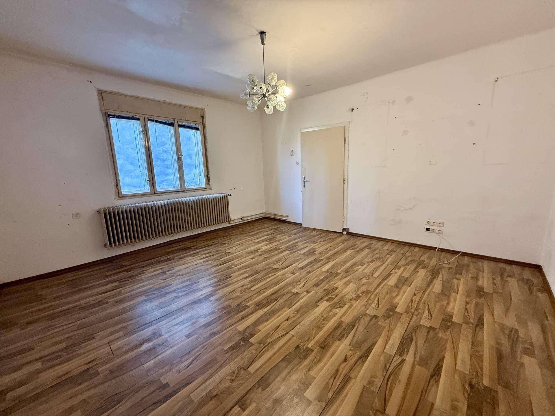 Geräumiges Zimmer mit Laminatboden, weißen Wänden und einem Fenster mit Heizkörper.