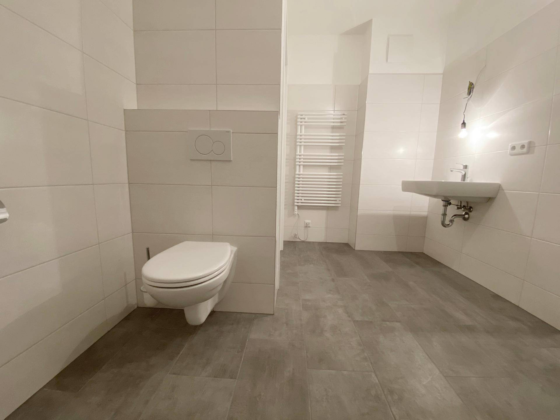 Modernes Badezimmer mit Wand-WC, Waschbecken, Handtuchheizkörper und großformatigen Fliesen.