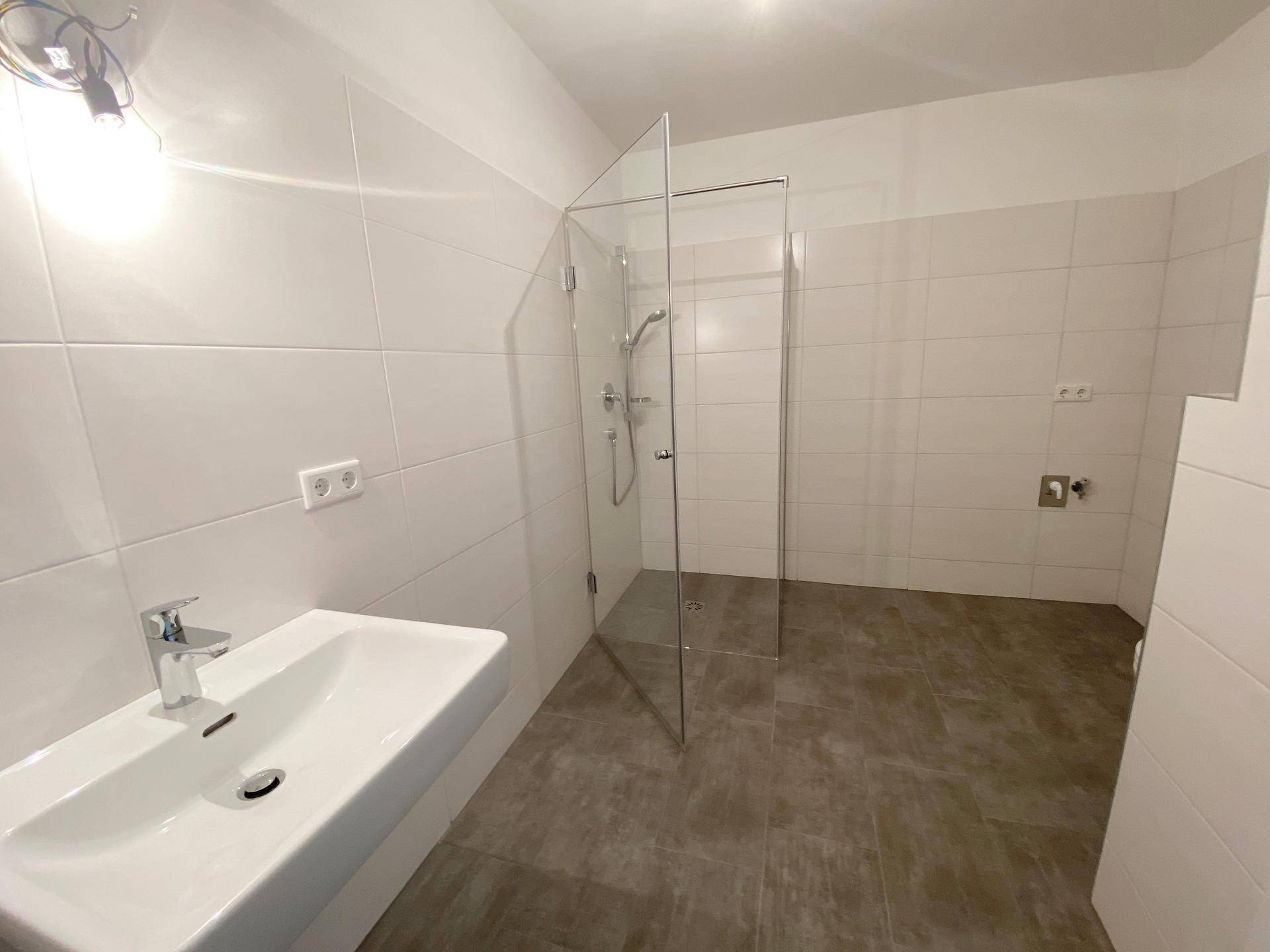 Helles Badezimmer mit begehbarer Dusche, Waschbecken und weißen Wandfliesen.