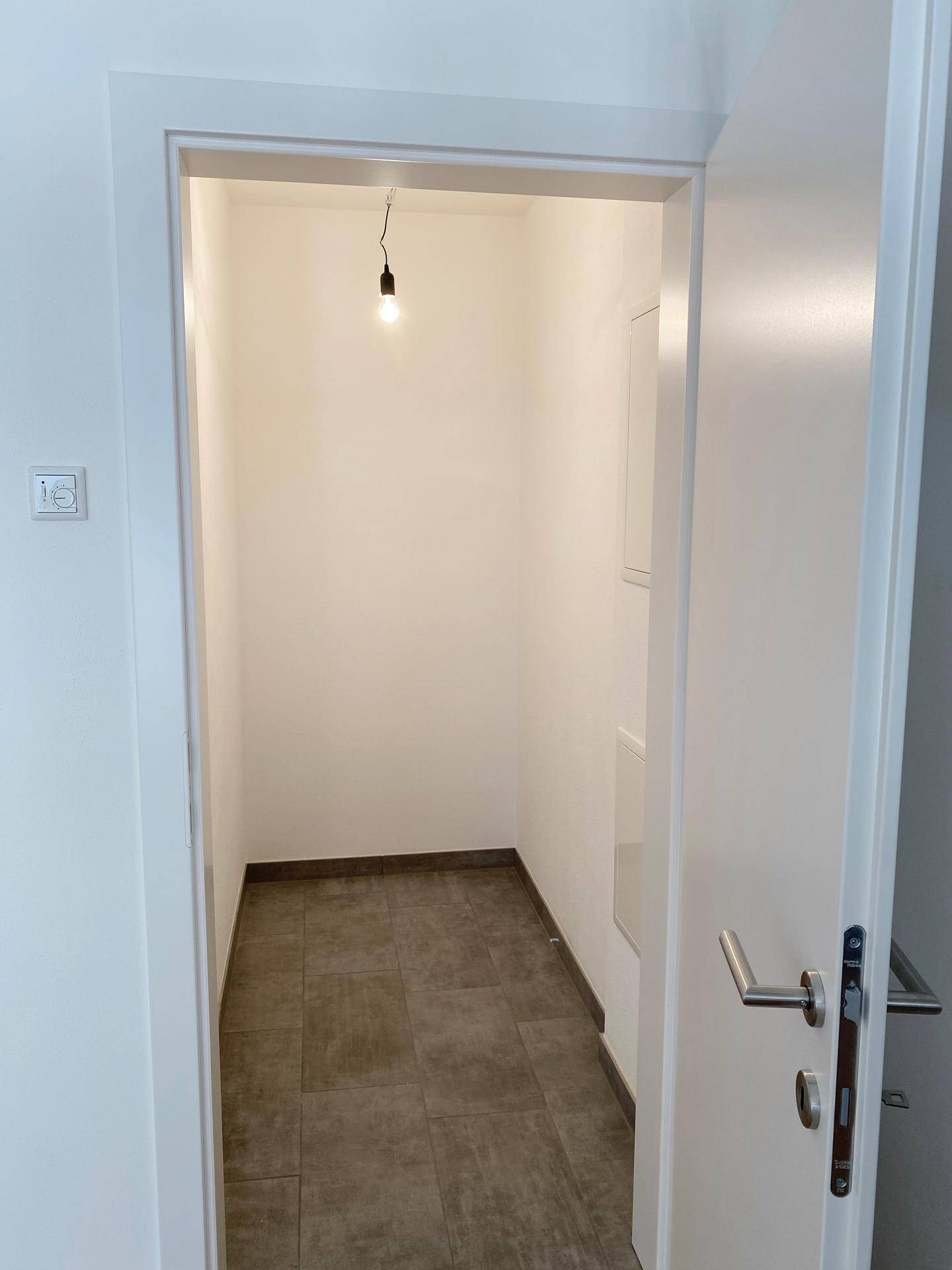 Praktischer Abstellraum mit Fliesenboden und weißen Wänden.