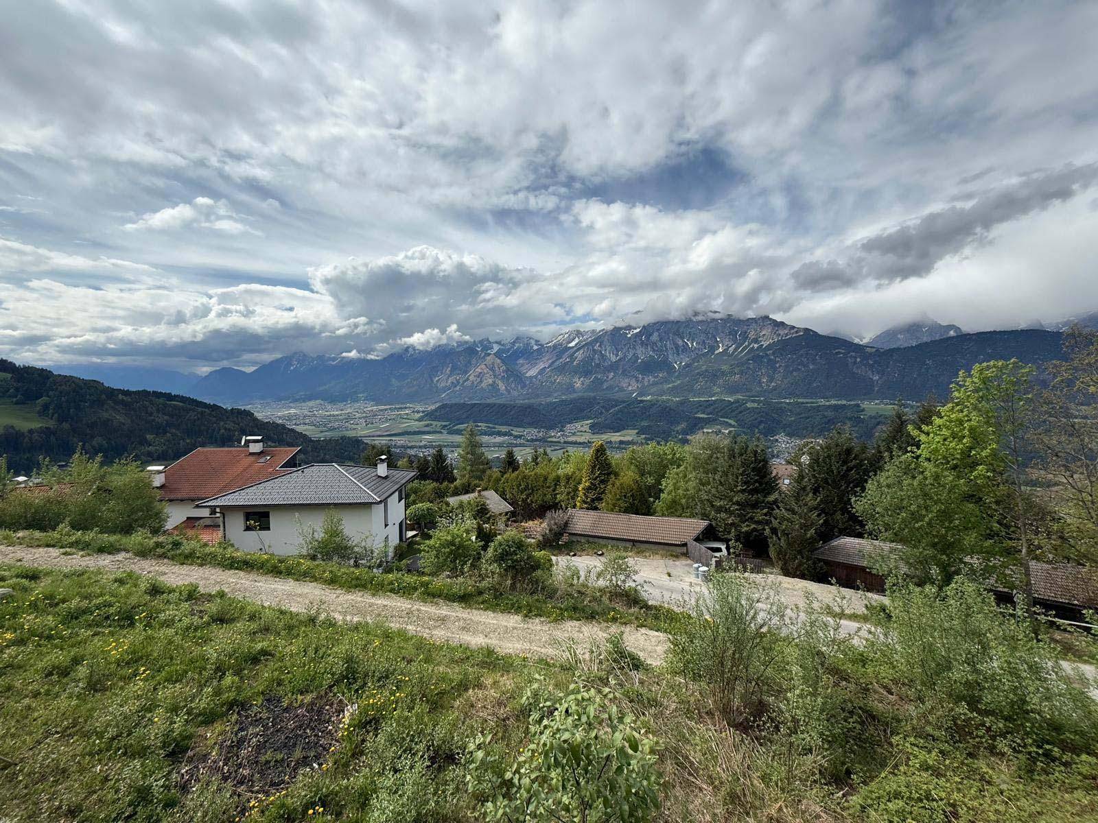 Weitläufiger Ausblick über das Tal mit Häusern und majestätischen Bergen unter einem bewölkten Himmel.