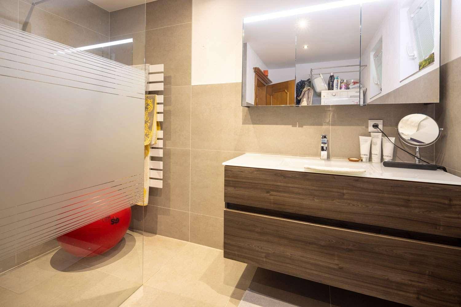 Modernes Badezimmer mit Holzwaschtisch, Spiegelschrank und begehbarer Dusche.