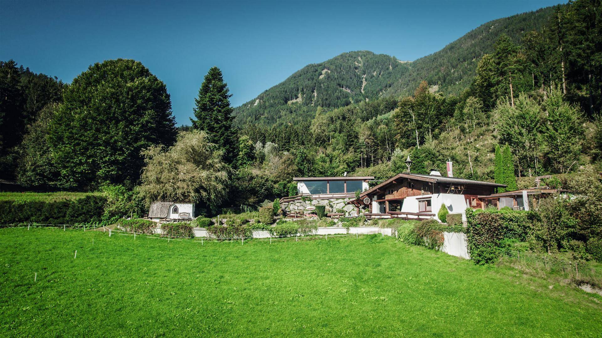 Charmantes Anwesen in alpiner Landschaft mit grünen Wiesen und bewaldeten Bergen im Hintergrund.