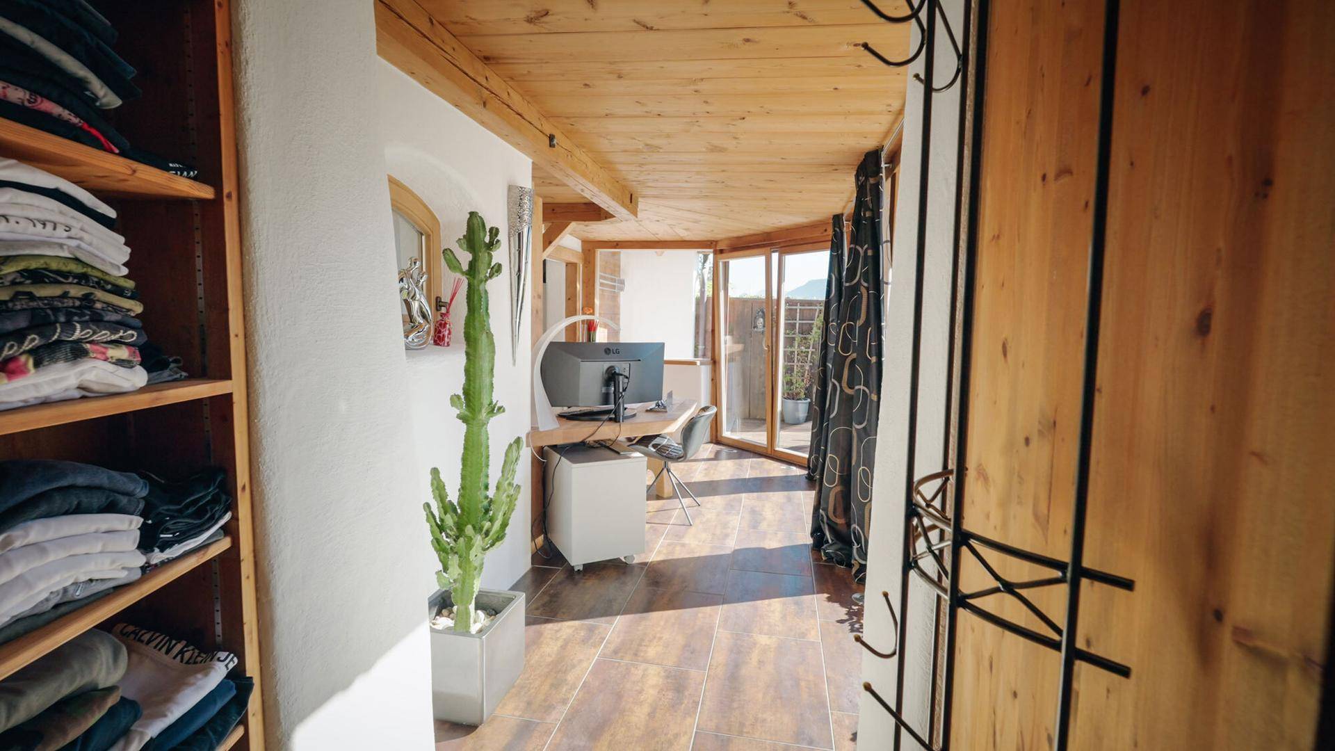Flur mit Holzregalen und Blick auf einen hellen Arbeitsbereich mit Terrassenzugang.