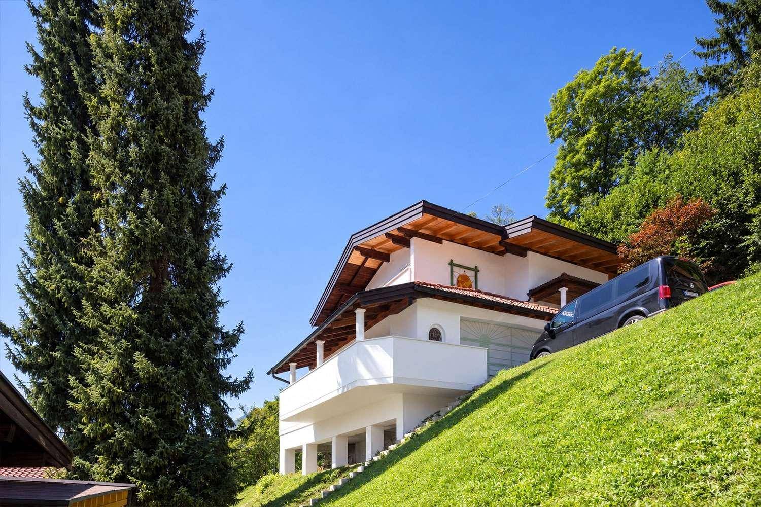 Attraktives Wohnhaus mit weißer Fassade, Balkonen und gepflegtem grünen Hanggrundstück.