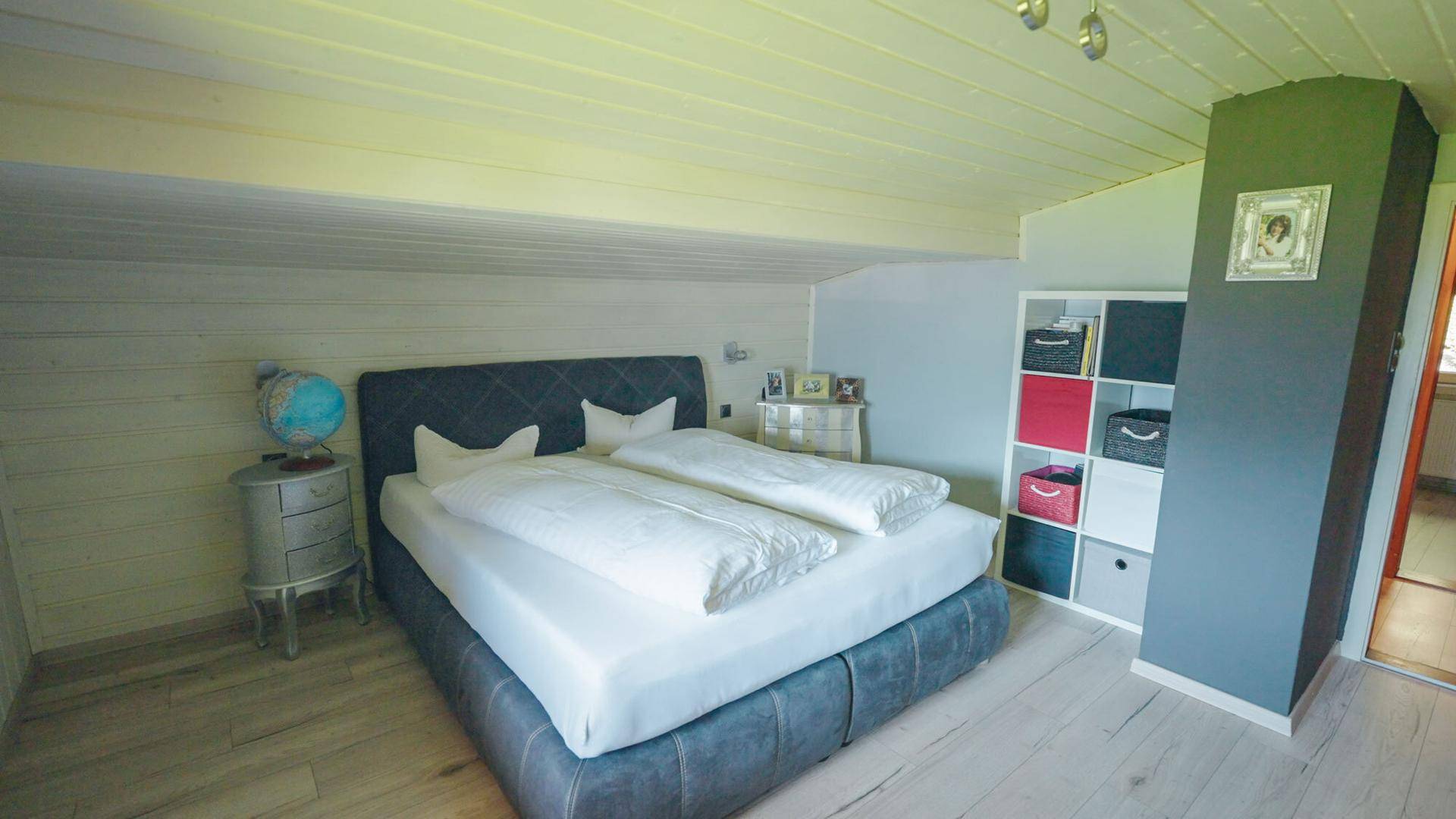 Helles Schlafzimmer im Dachgeschoss mit Holzbalkendecke und modernem Bett.