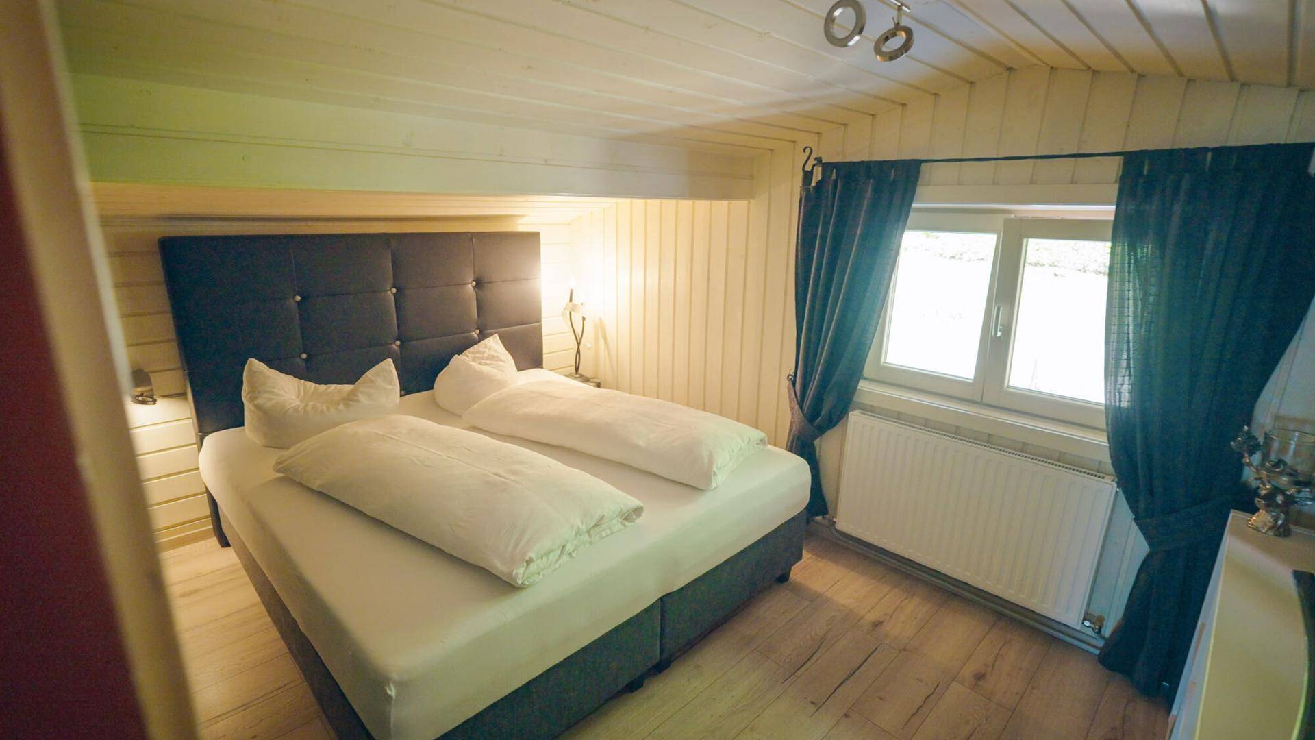 Schlafzimmer mit Holzboden, Doppelbett und Fenster mit Blick ins Grüne.