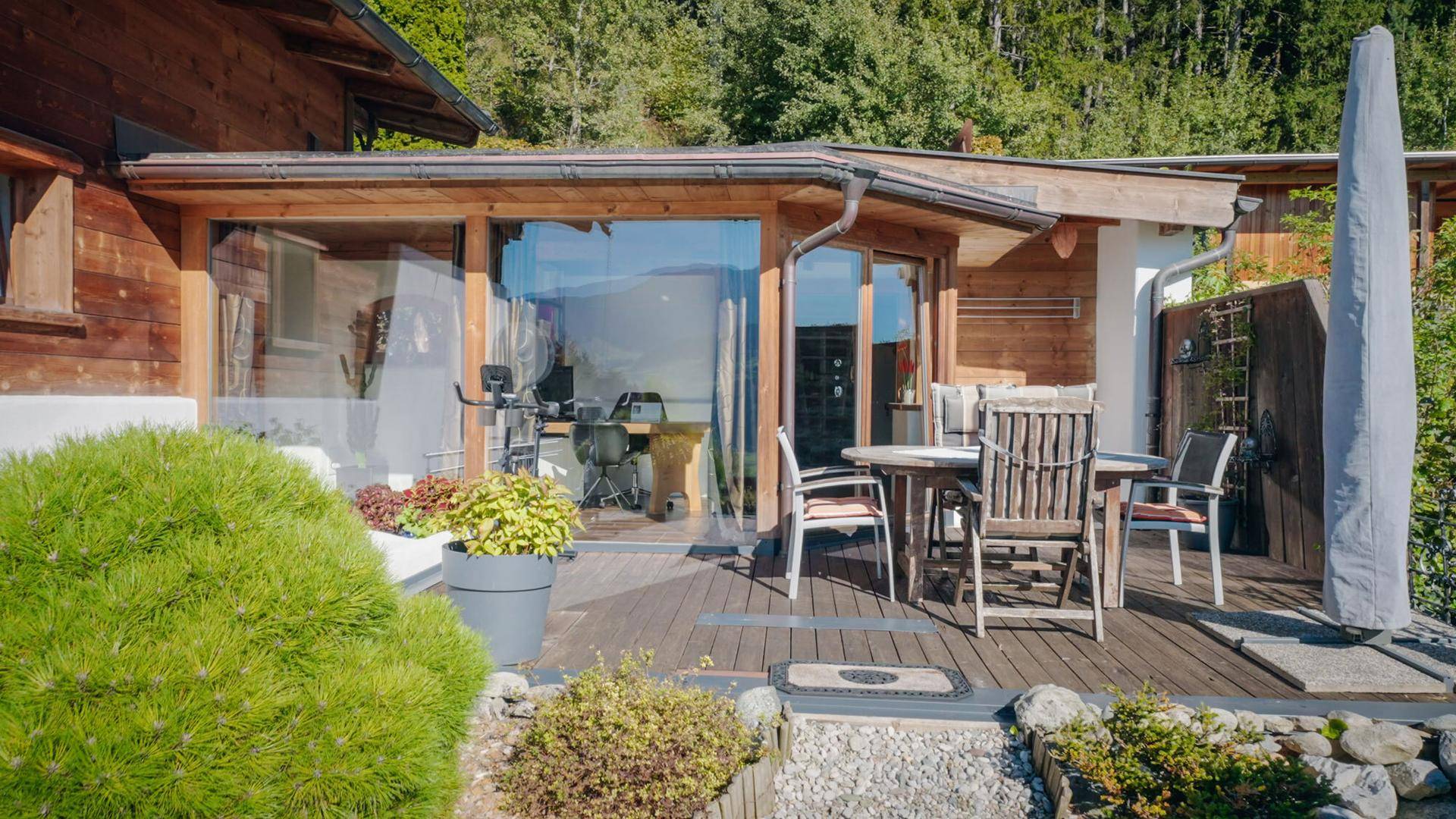 Holzterrasse mit Gartenmöbeln und Zugang zu den Innenräumen, umgeben von Grün.