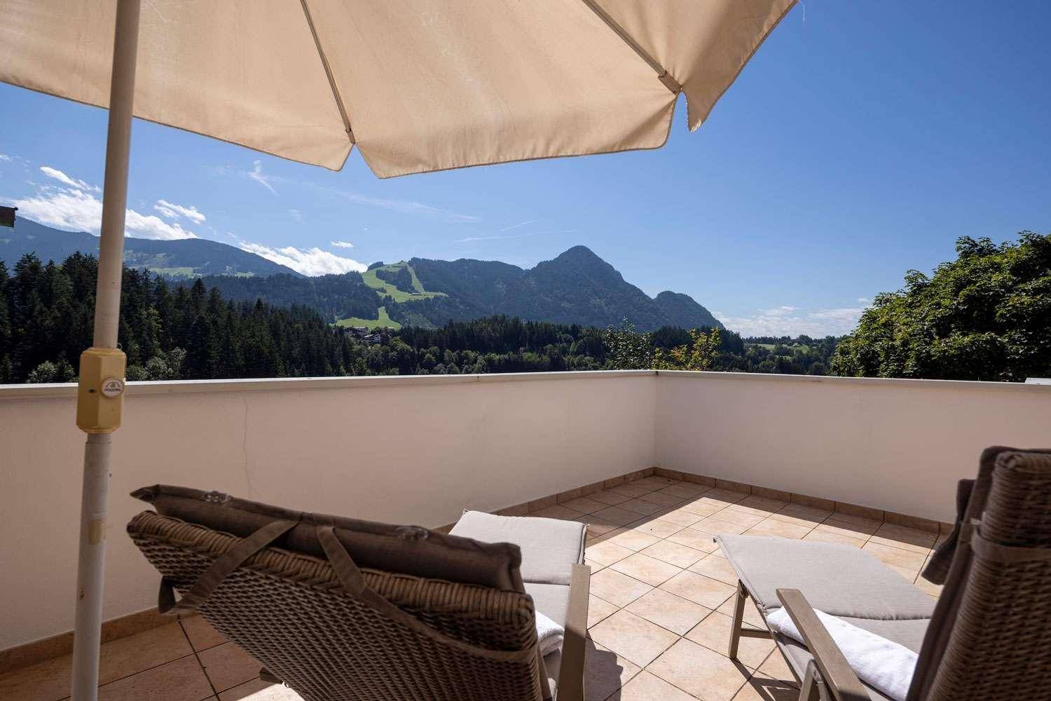 Sonnenterrasse mit Liegestühlen und Sonnenschirm, ideal zum Entspannen mit Bergblick.