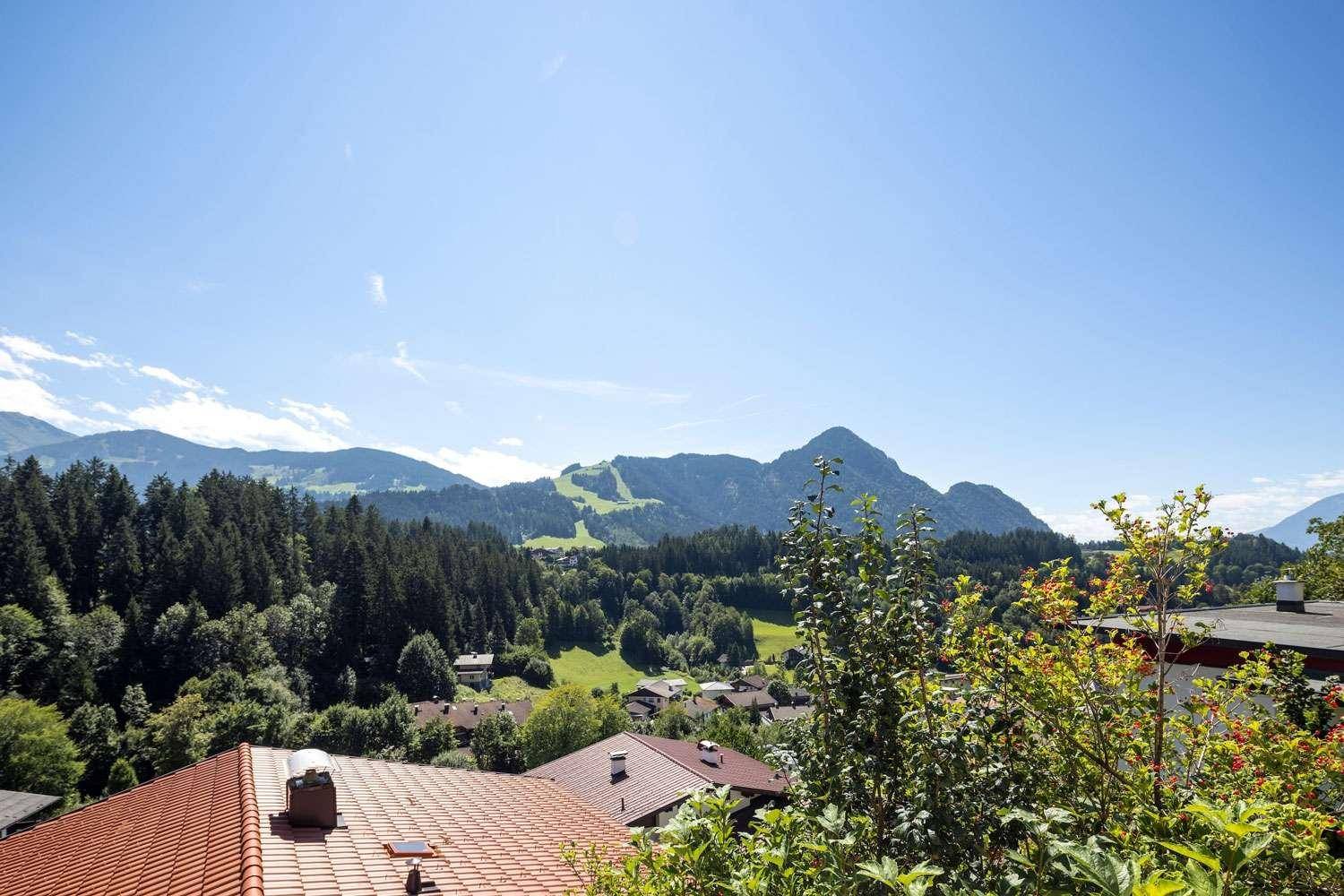 Panoramablick auf die majestätischen Berge und das grüne Tal mit vereinzelten Häusern.