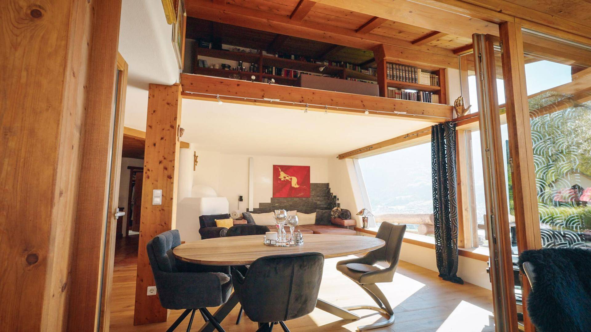Heller Wohn-Essbereich mit hoher Decke, Holzdetails und einer Galerie mit Bücherregalen.