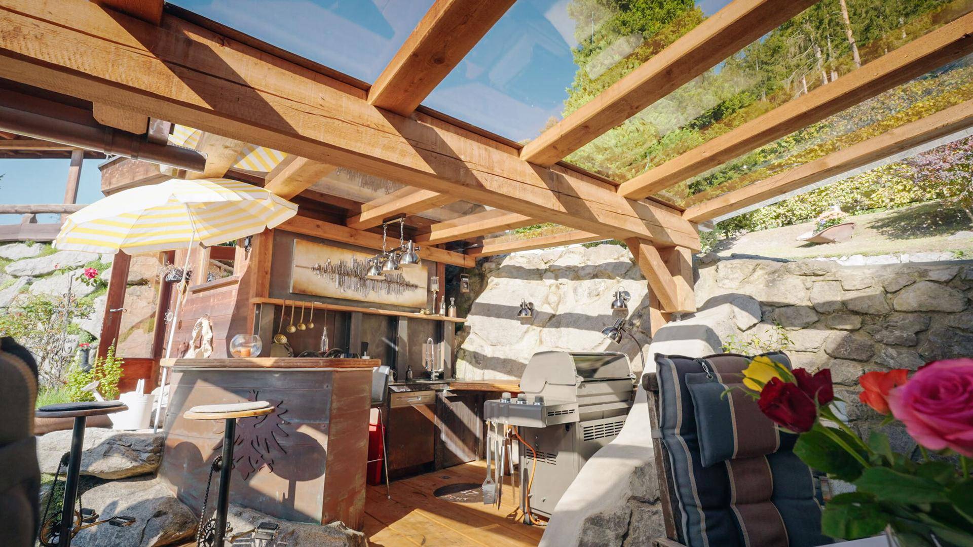 Überdachte Außenküche mit Grillbereich und Bar, umgeben von Steinmauern.