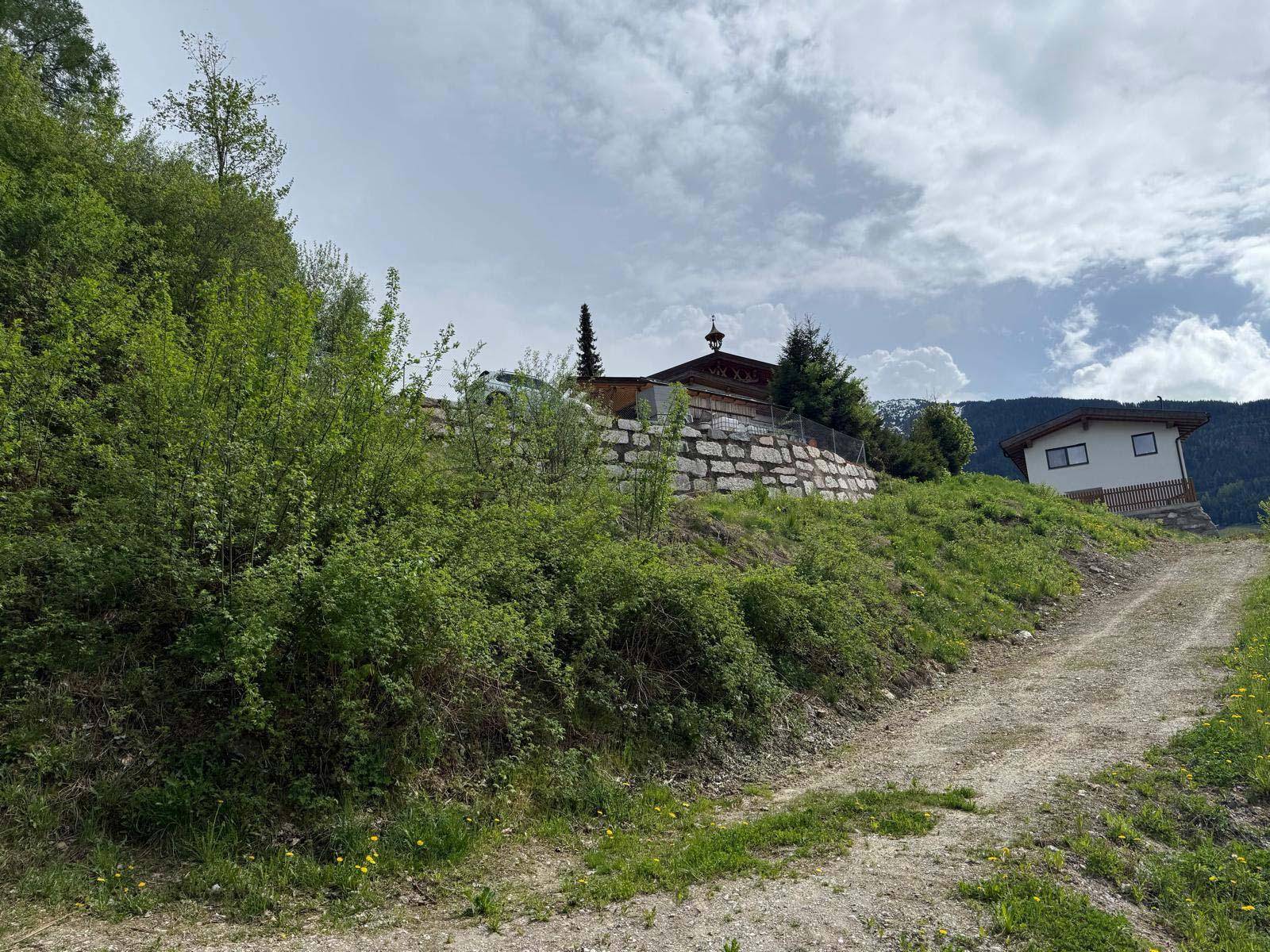 Hanggrundstück mit einer Steinmauer und einem unbefestigten Weg, umgeben von grüner Natur.