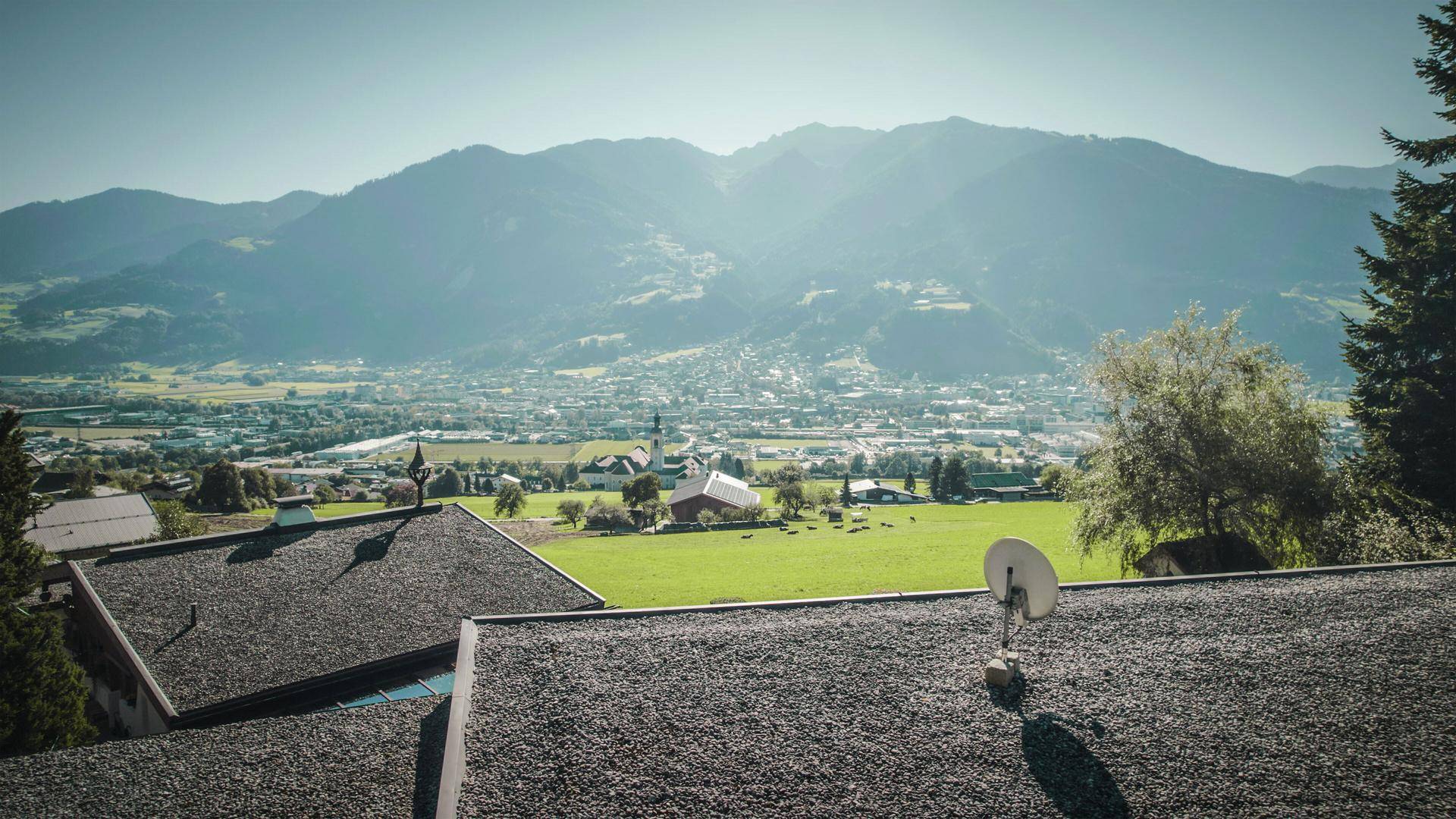 Weitblick über das Tal und eine Stadt im Hintergrund, umgeben von majestätischen Bergen.