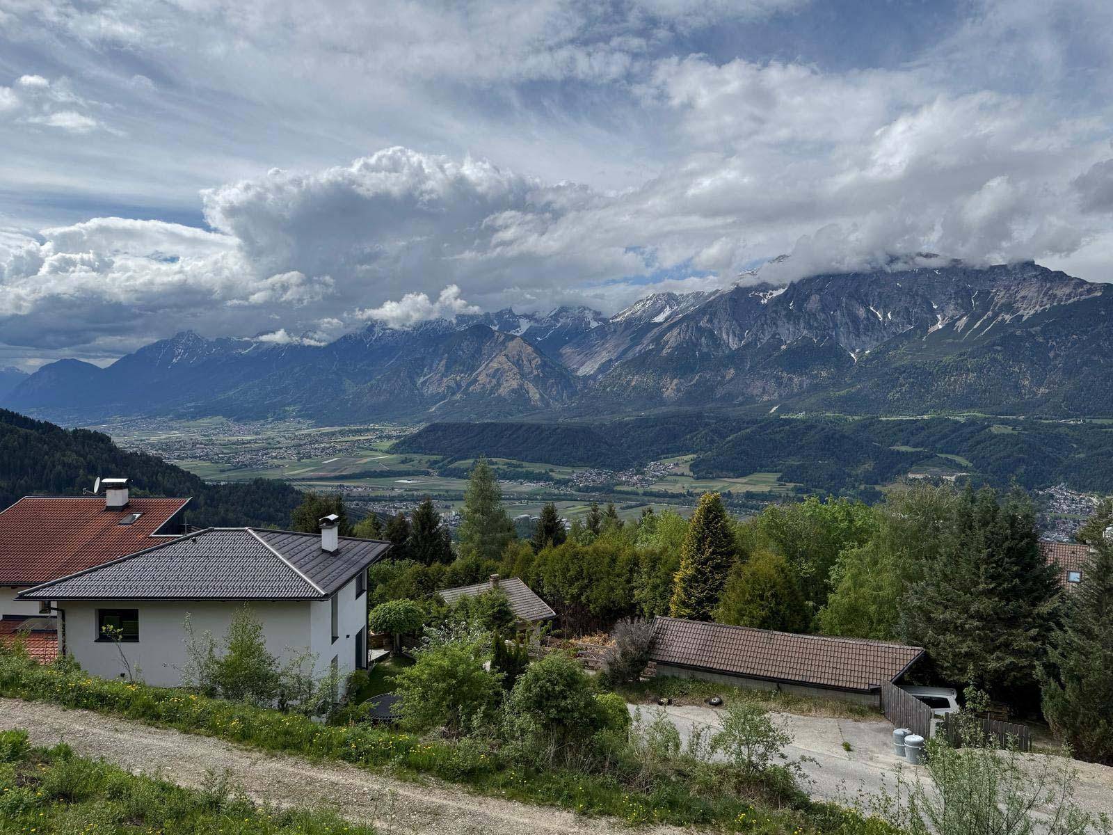 Panoramablick auf die Bergwelt und das Tal, mit einem Wohnhaus im Vordergrund und bewölktem Himmel.