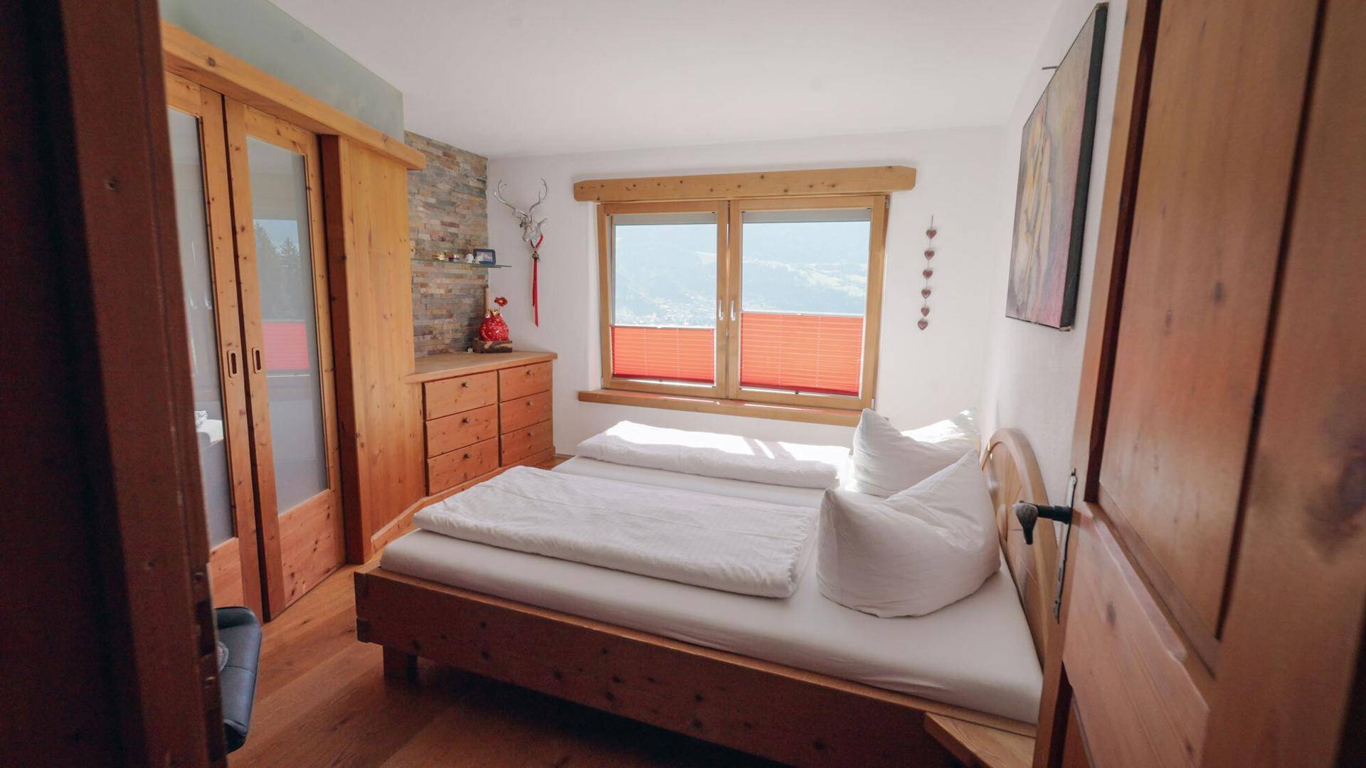 Gemütliches Schlafzimmer mit Holzbett, Schrank und Fenster mit Bergblick.