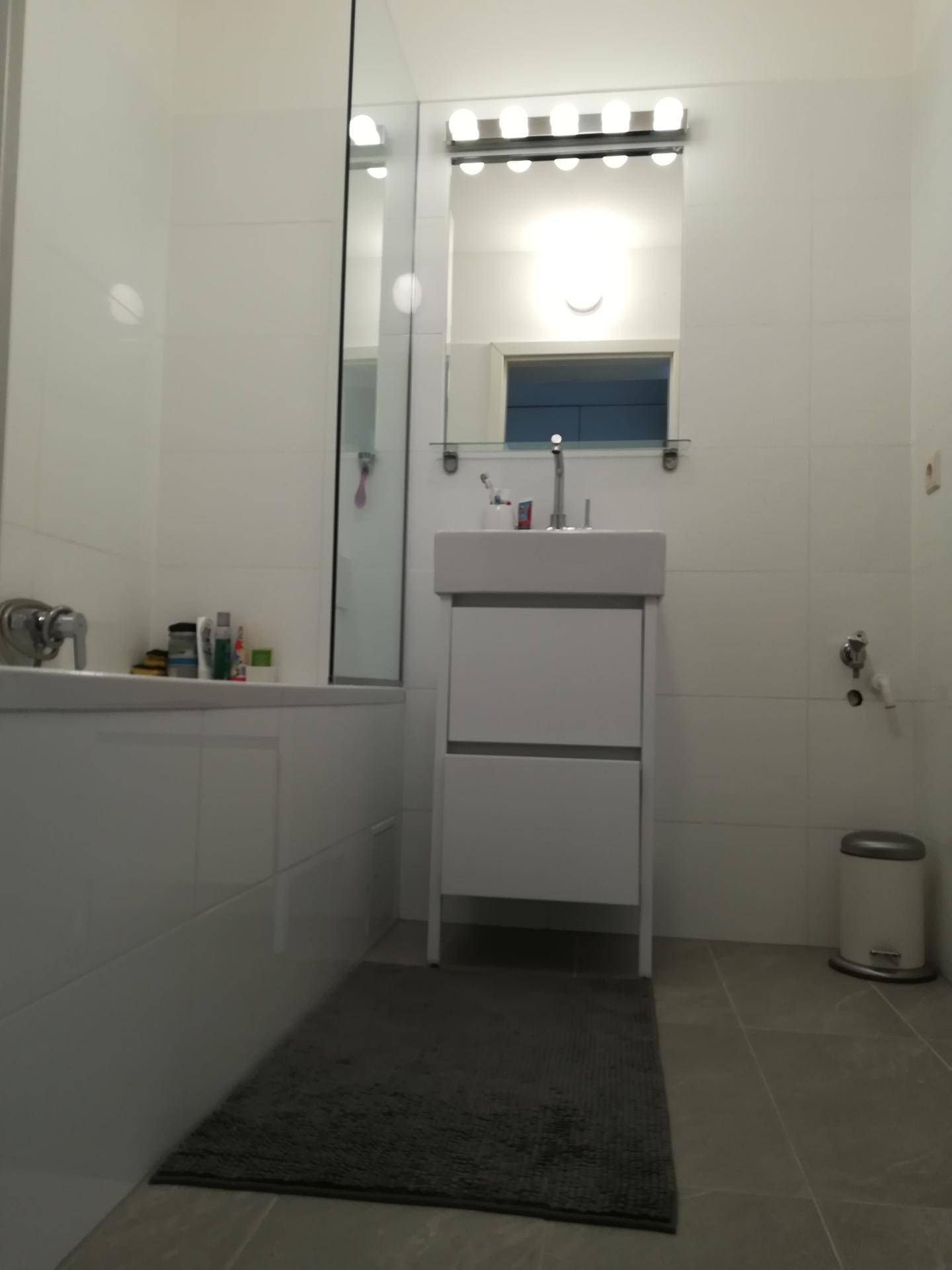 Modernes Badezimmer mit Badewanne, Waschtisch und großen weißen Wandfliesen.