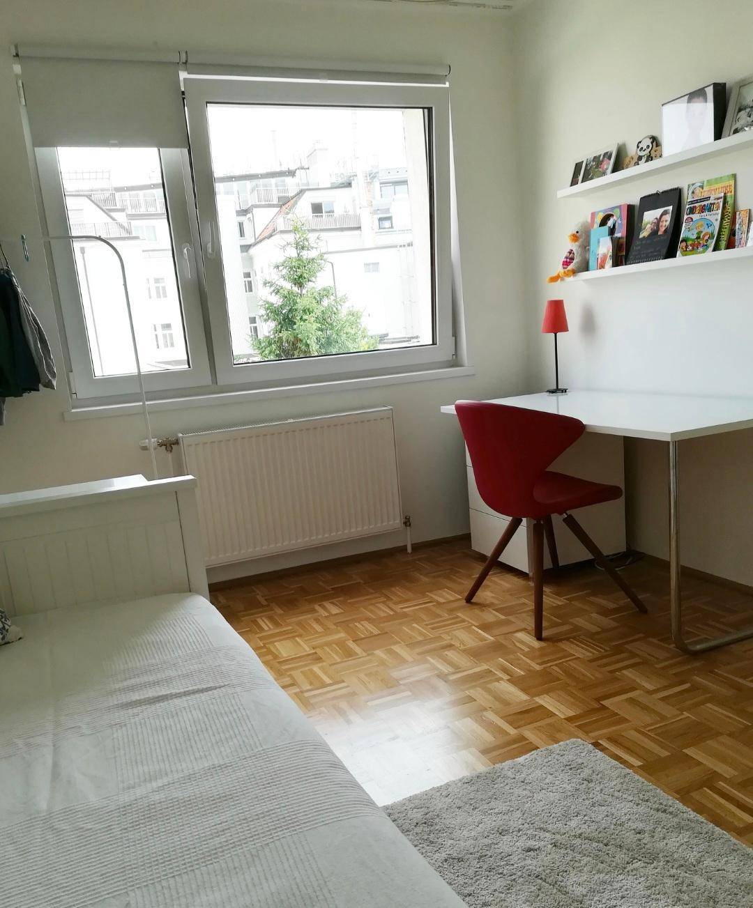 Helles Schlafzimmer mit Parkettboden, Schreibtisch und Blick ins Grüne.