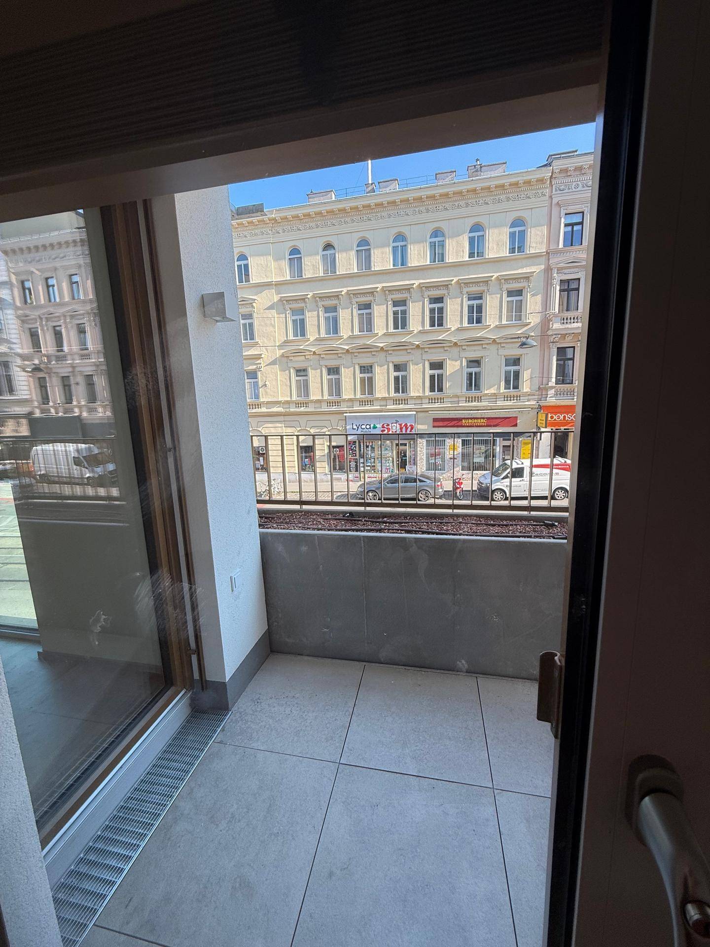 Kleiner Balkon mit Fliesenboden und Blick auf die gegenüberliegende Straße und Gebäude.