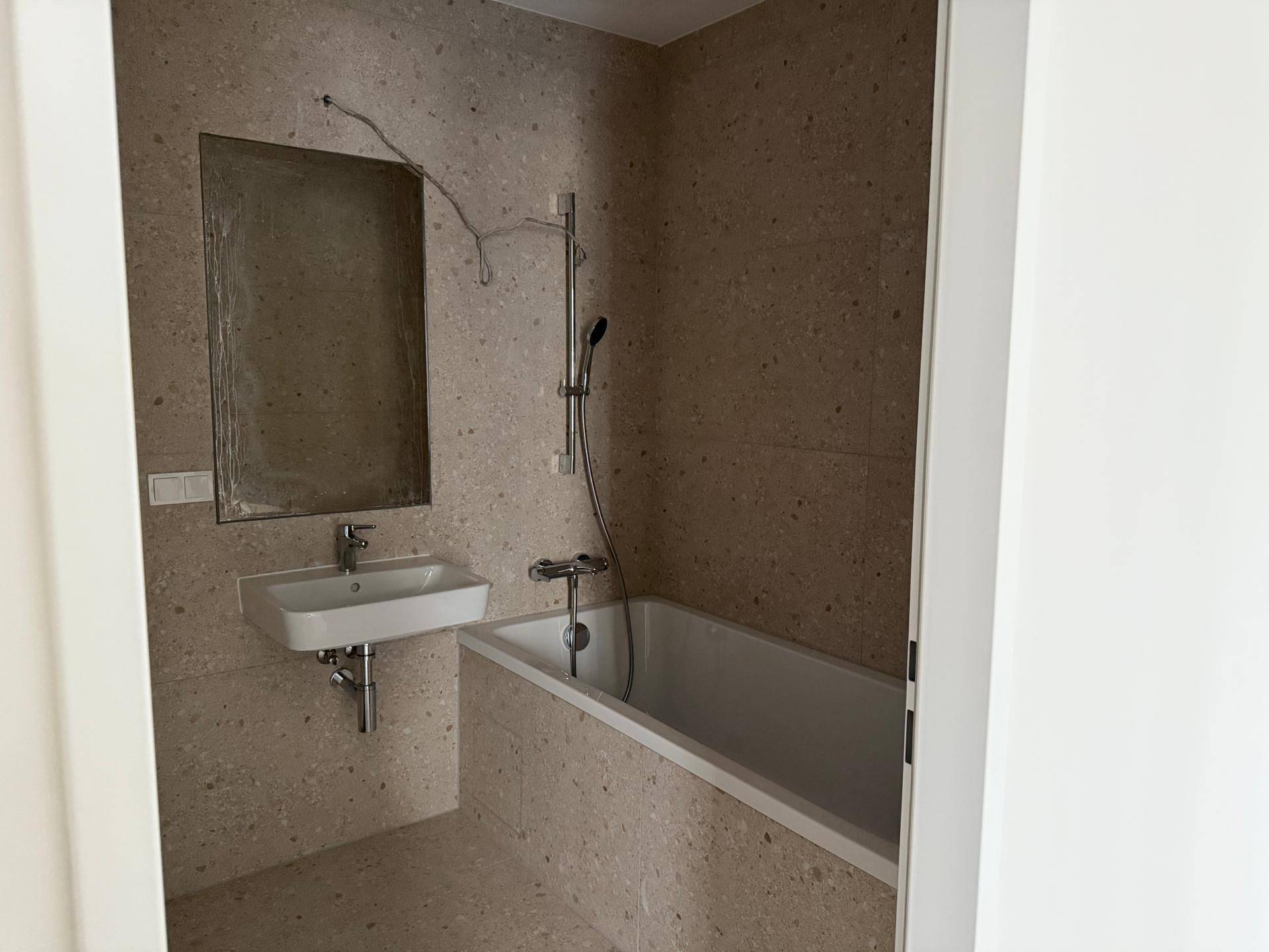 Badezimmer mit Badewanne, Waschbecken und gefliesten Wänden in neutralen Farbtönen.