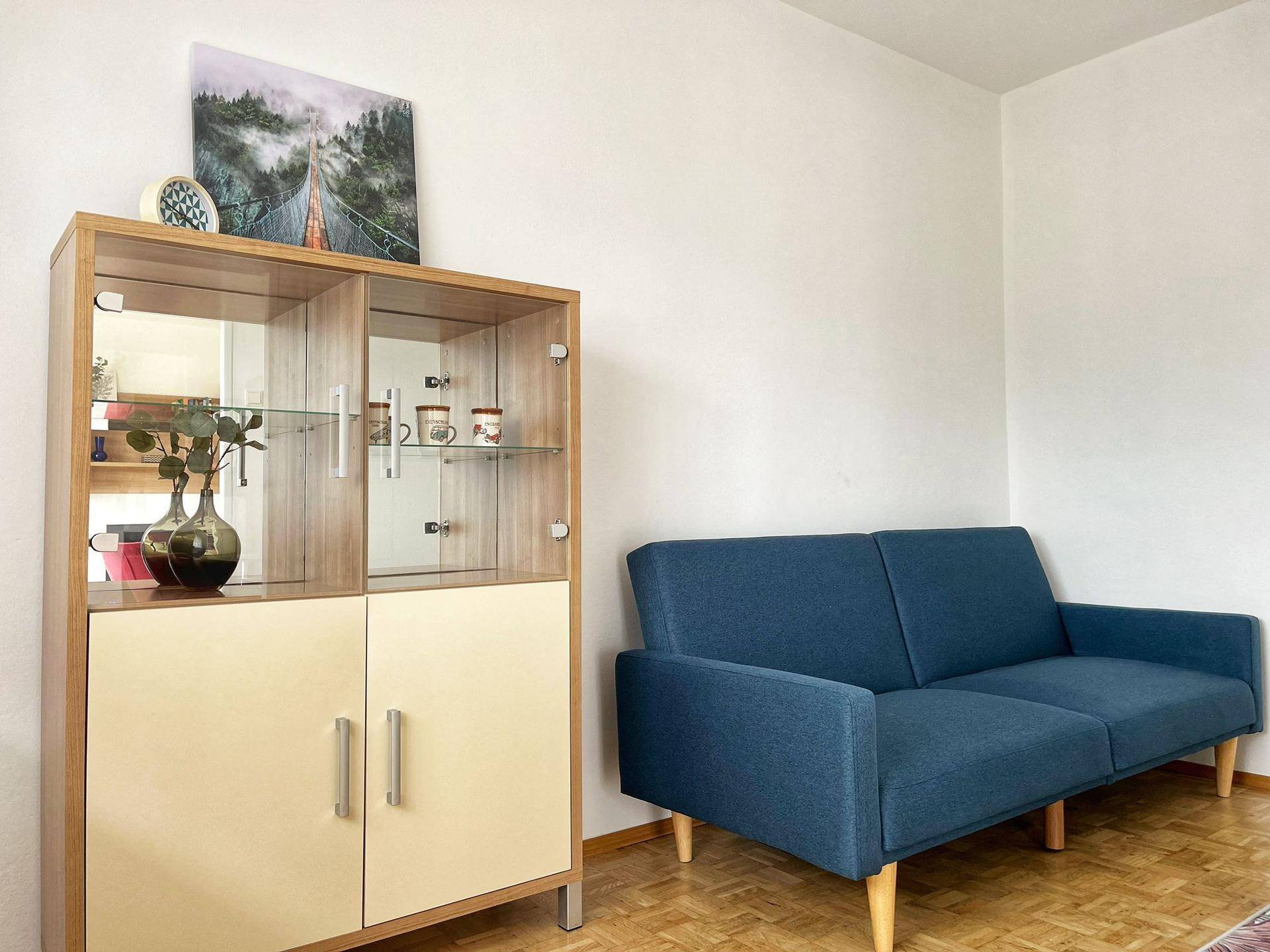 Helles Wohnzimmer mit bequemer blauer Couch und stilvollem Vitrinenschrank.