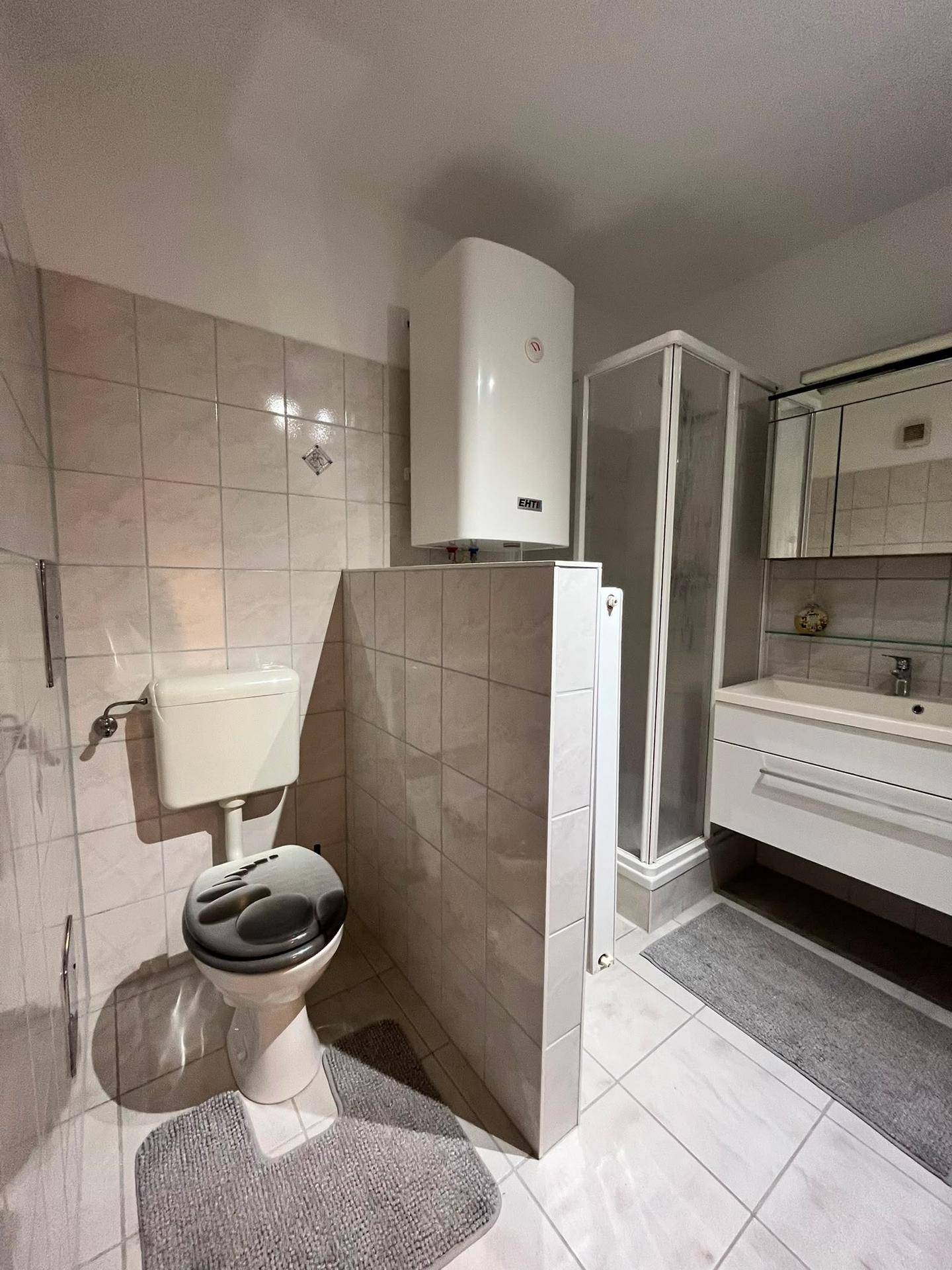 Badezimmer mit Toilette, Duschkabine und Waschbecken in hellen Fliesen.