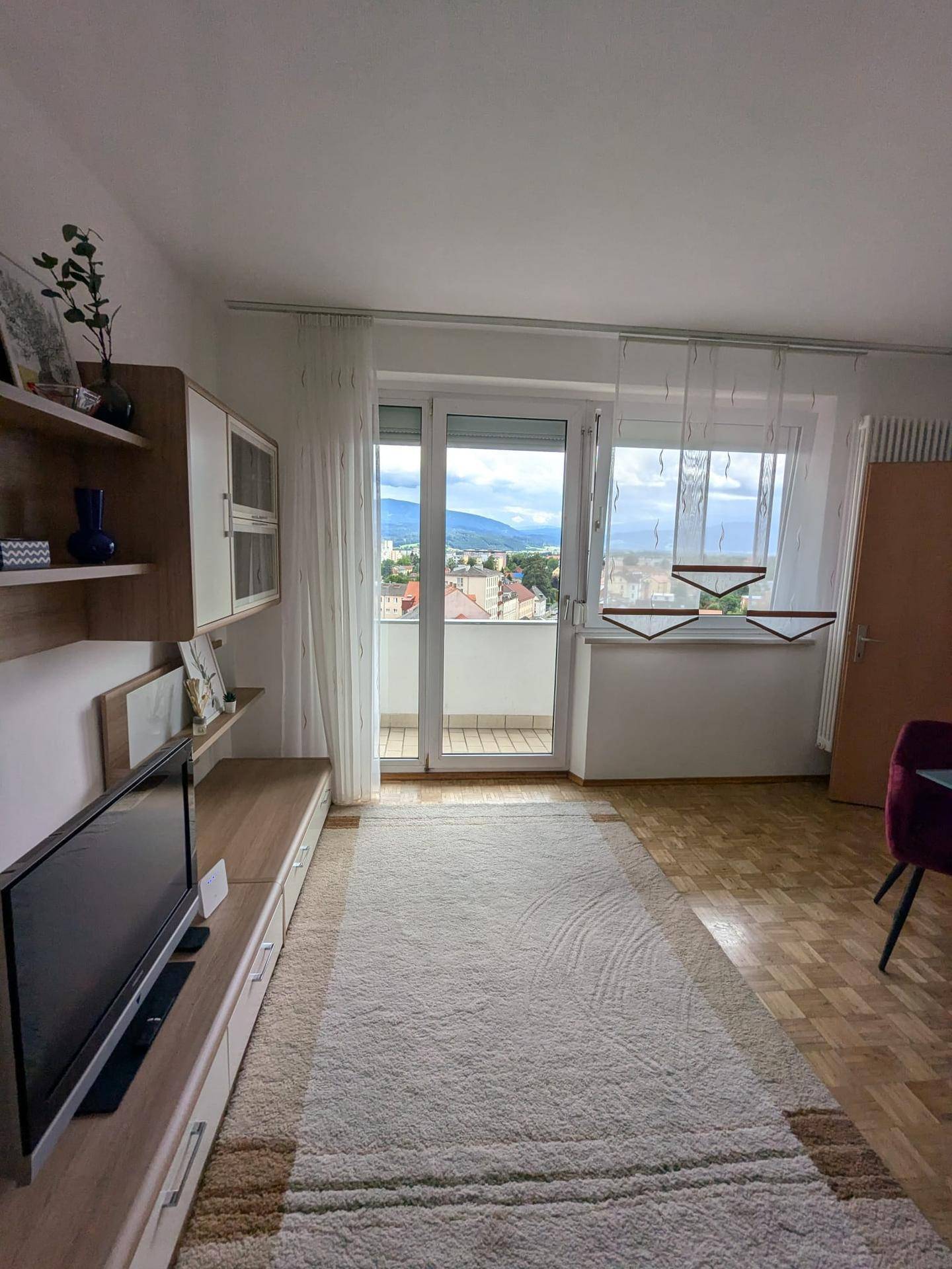 Wohnzimmer mit TV-Möbeln, Teppich und Zugang zu einem Balkon mit schöner Aussicht.
