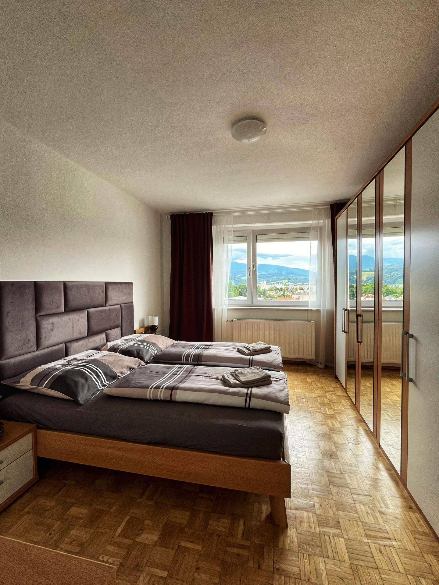 Gemütliches Schlafzimmer mit zwei Einzelbetten, Parkettboden und einem Fenster mit Bergblick.