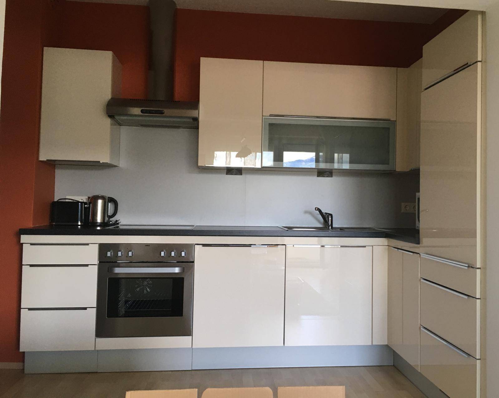 Moderne Einbauküche mit beigen Hochglanzfronten, integriertem Backofen und Dunstabzugshaube.