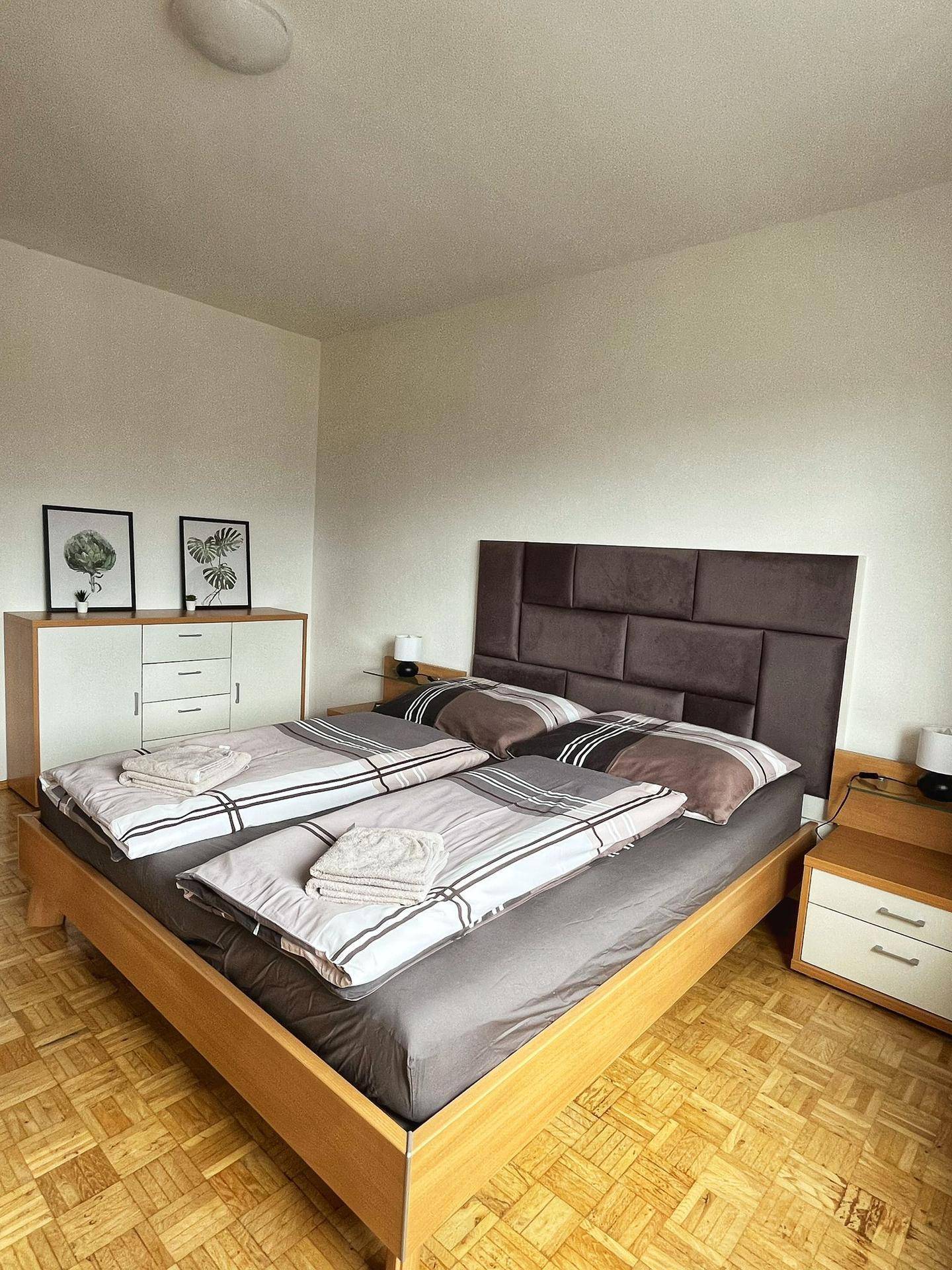 Helles Schlafzimmer mit bequemen Betten, Parkettboden und einem modernen Sideboard.