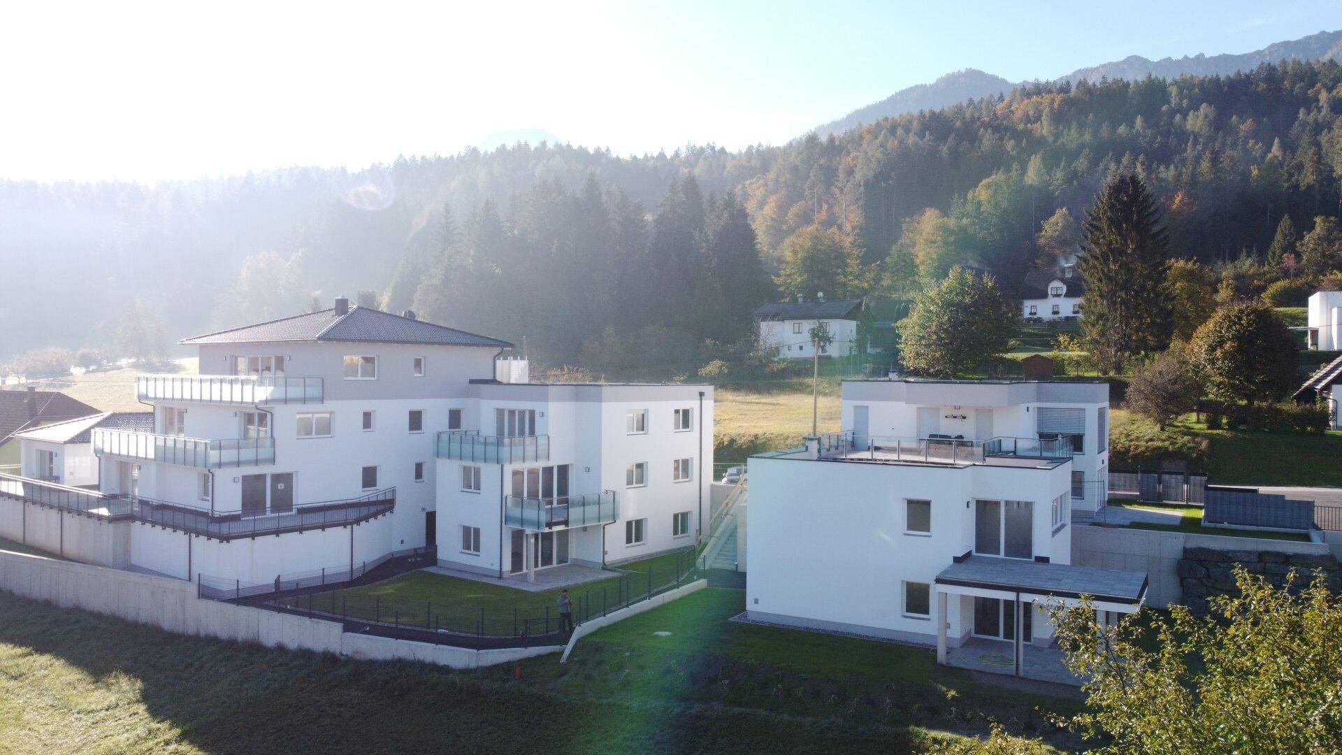 Luftaufnahme einer modernen Wohnanlage eingebettet in eine grüne, hügelige Landschaft.