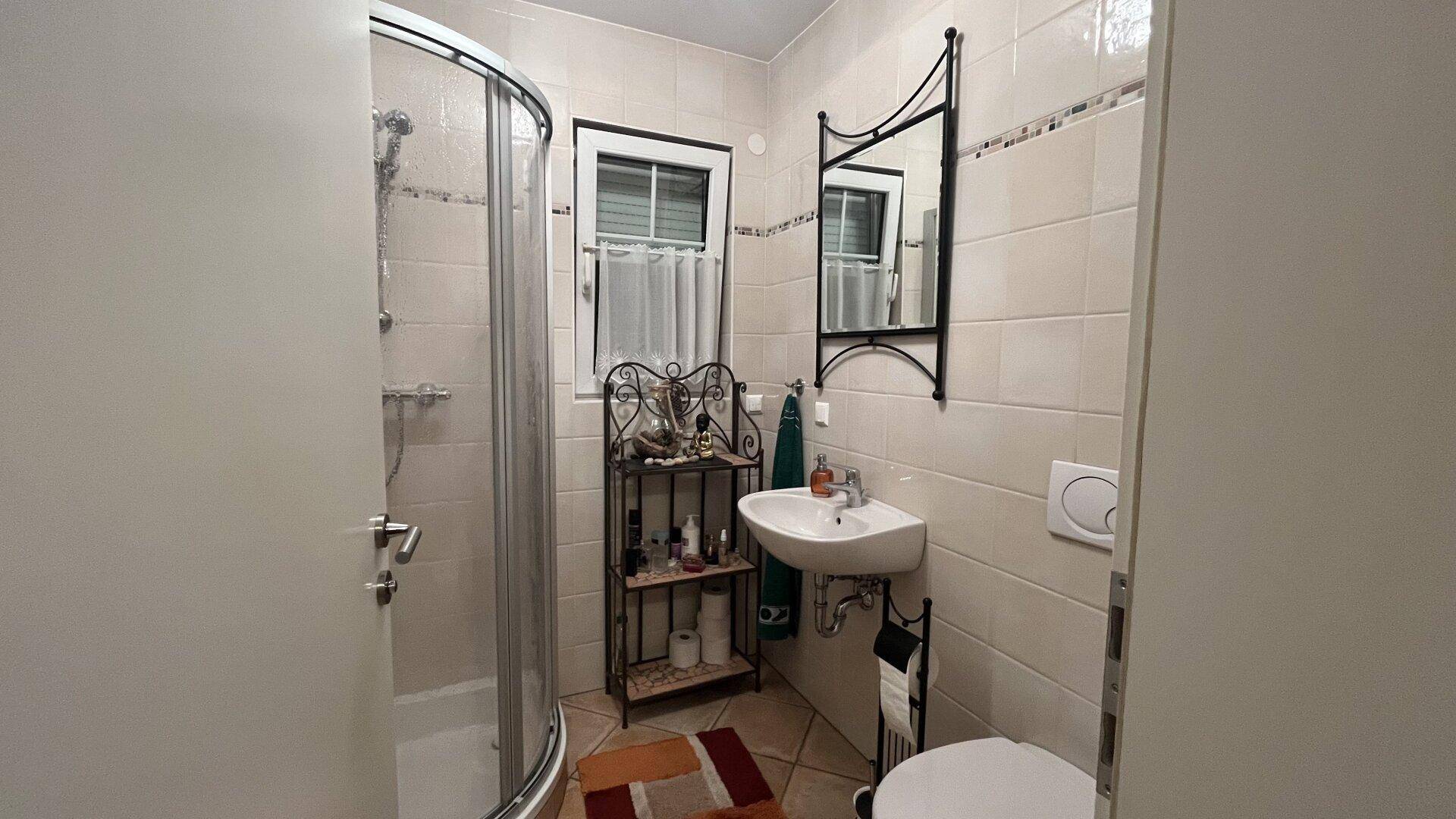 Kleines Badezimmer mit Duschkabine, Waschbecken und WC, hell gefliest.