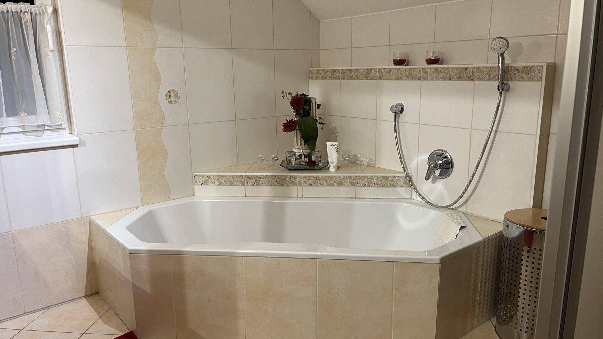 Badezimmer mit großer Eckbadewanne und Duschvorrichtung, hell gefliest.