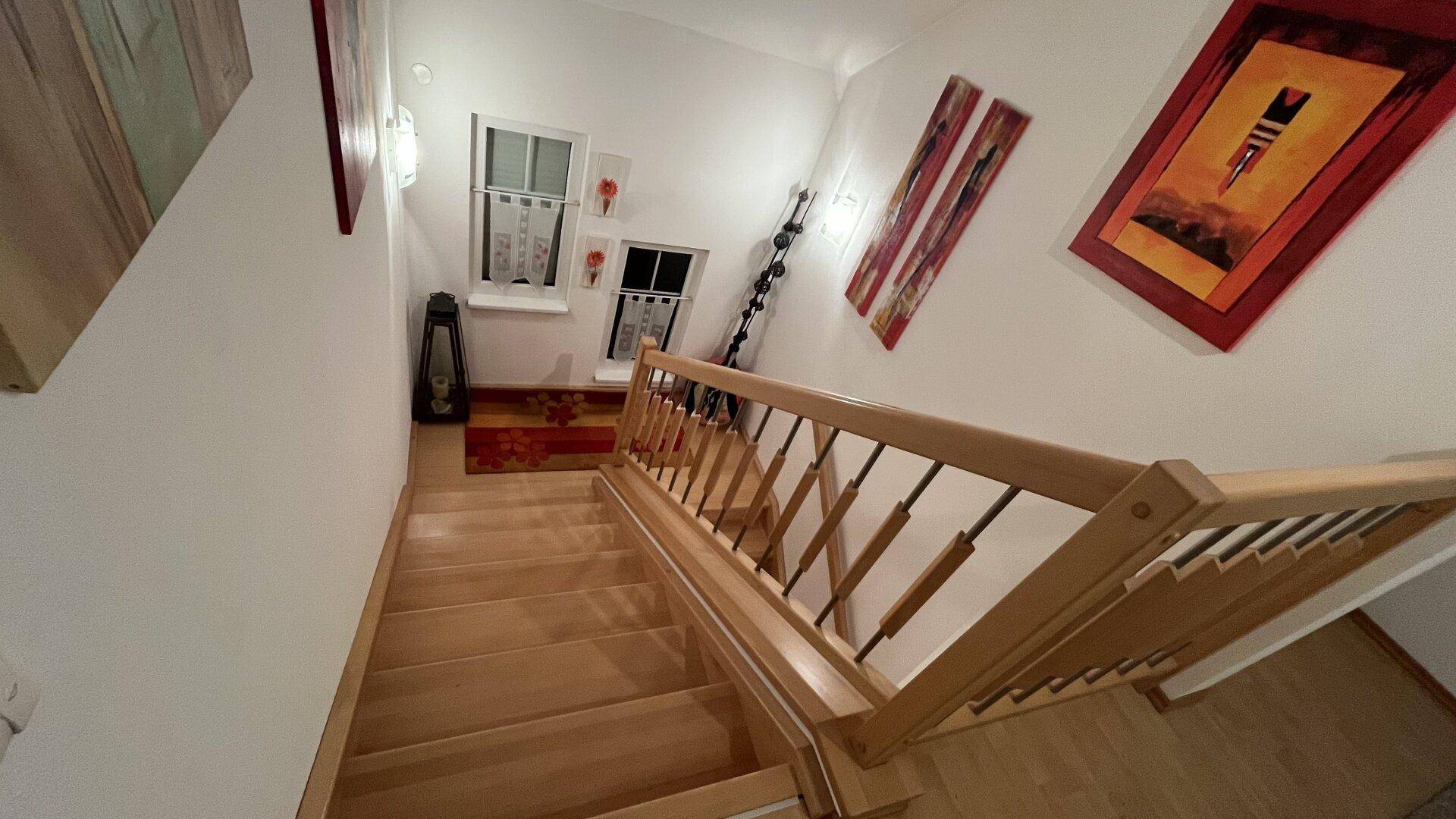 Helle Holztreppe führt in die obere Etage, mit dekorativen Bildern an der Wand.