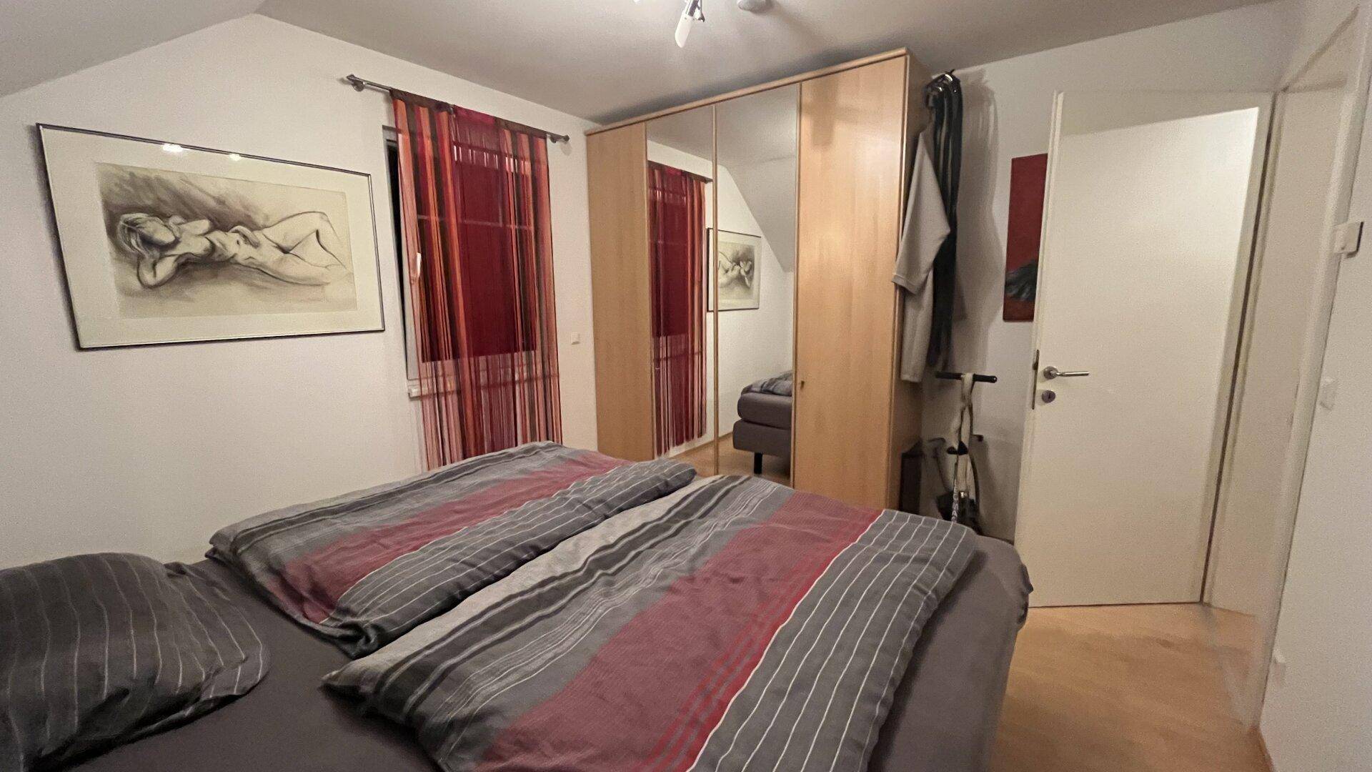 Schlafzimmer mit Doppelbett, Spiegelschrank und Fenster mit roten Vorhängen.