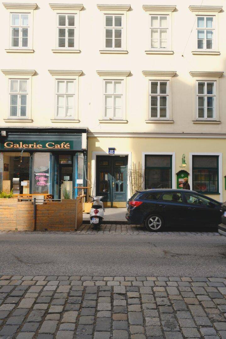 Historische Fassade eines Gebäudes mit Galerie-Café und parkenden Autos auf der Straße.